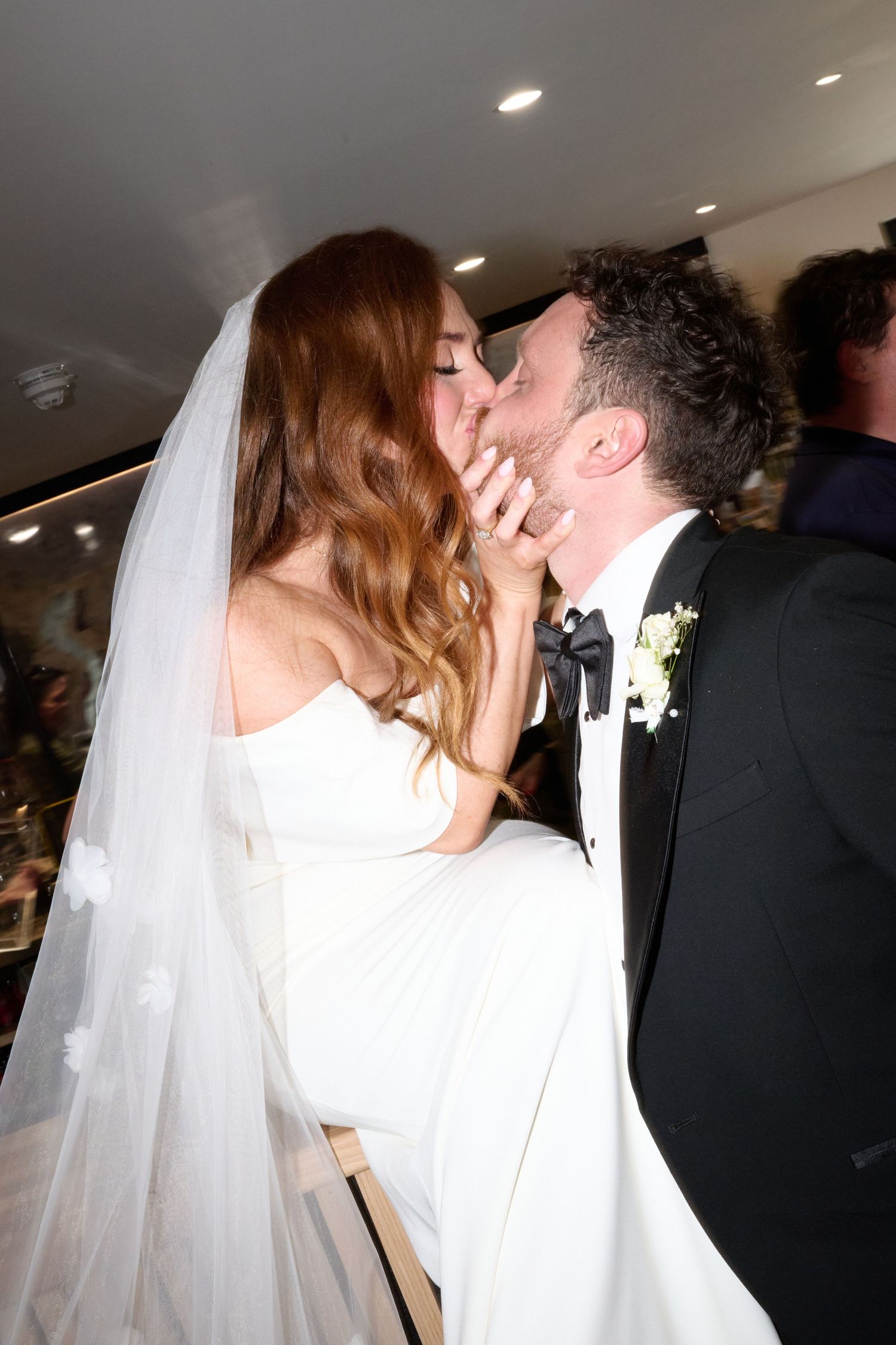 Bride and groom share a romantic first kiss at their wedding ceremony, bride wearing white gown and veil.