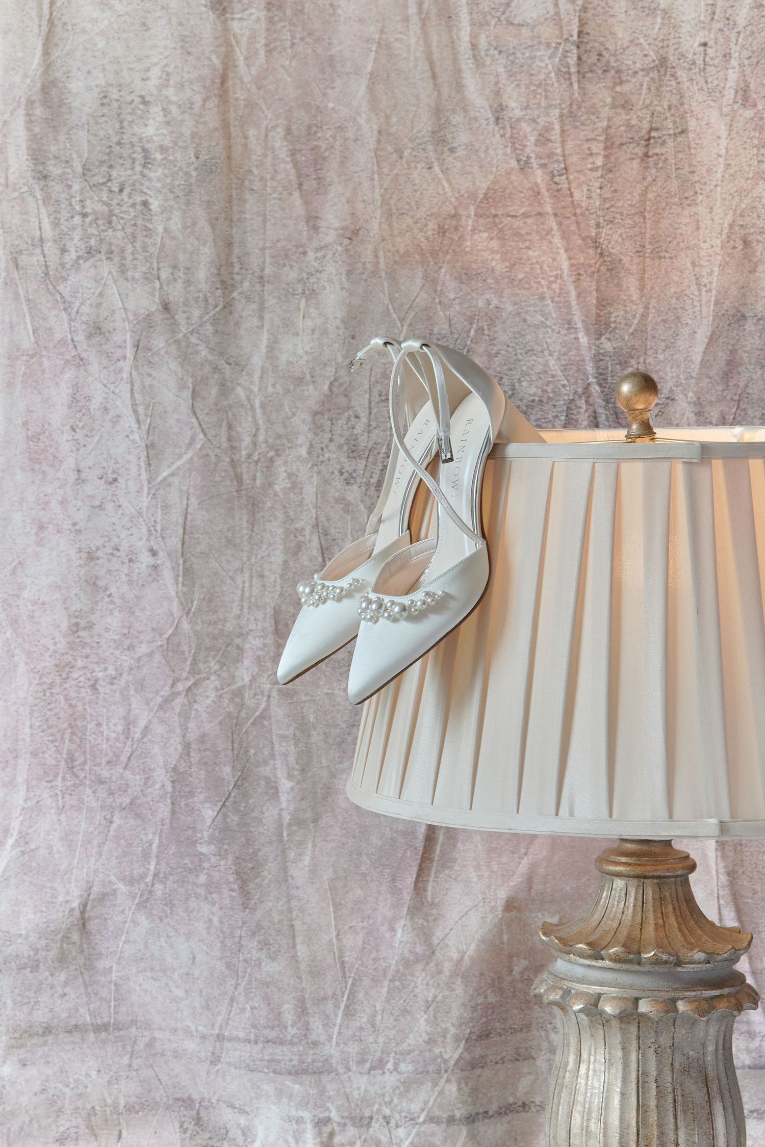 White bridal heels with crystal embellishments hanging delicately on a decorative lamp shade.