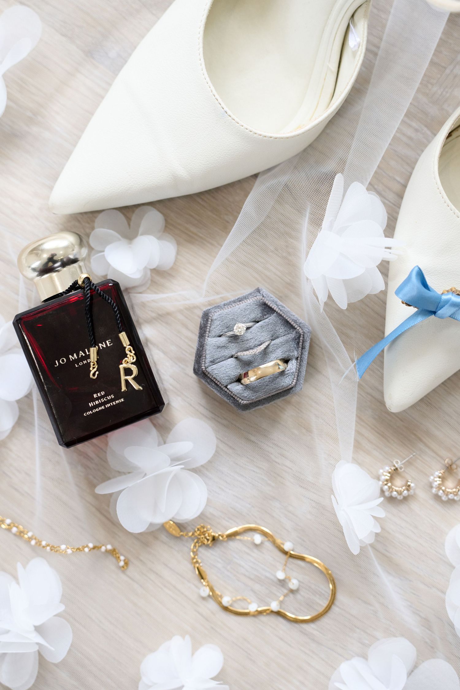 Elegant bridal flat lay with Jo Malone perfume, wedding rings, pearl jewelry, white heels, and floral veil details.
