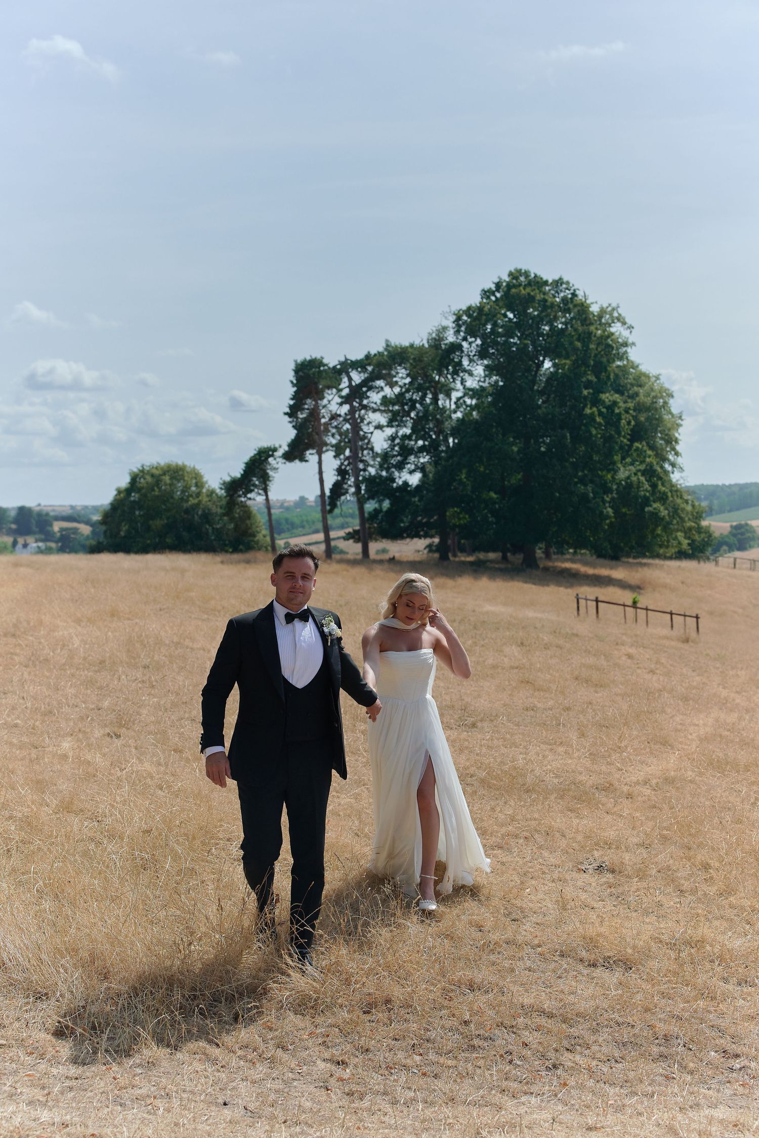 Bride and groom walking hand in hand through golden fields on their wedding day.