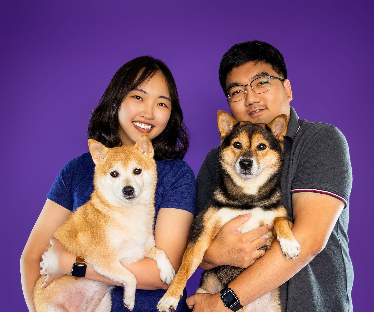 Smiling couple holds two Shiba Inu dogs on a purple studio background - professional dog photography in London, Ontario | Paws Photos