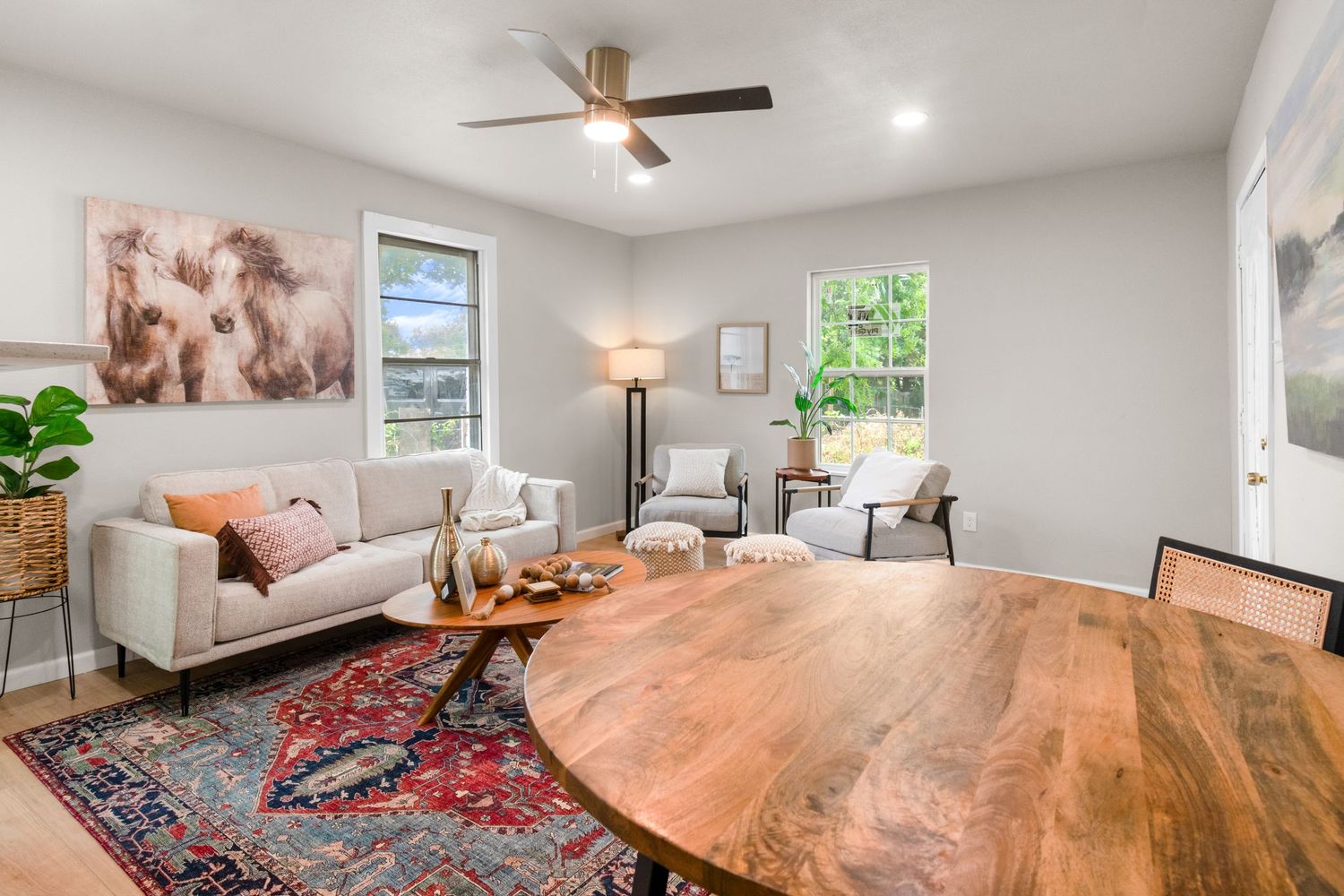 Bright living room with white sofa, wooden coffee table, red Persian rug, ceiling fan, and large windows with natural light.