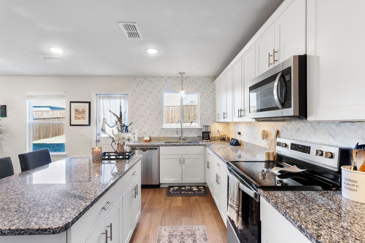 Modern kitchen with white cabinets, granite countertops, stainless steel appliances, and herringbone tile backsplash over hardwood floors.