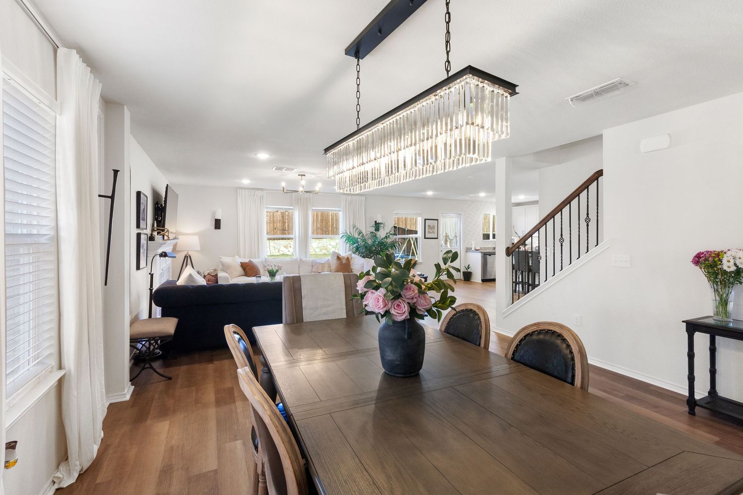 Elegant dining room with crystal chandelier, dark wood table, hardwood floors, and open view to living room and staircase.