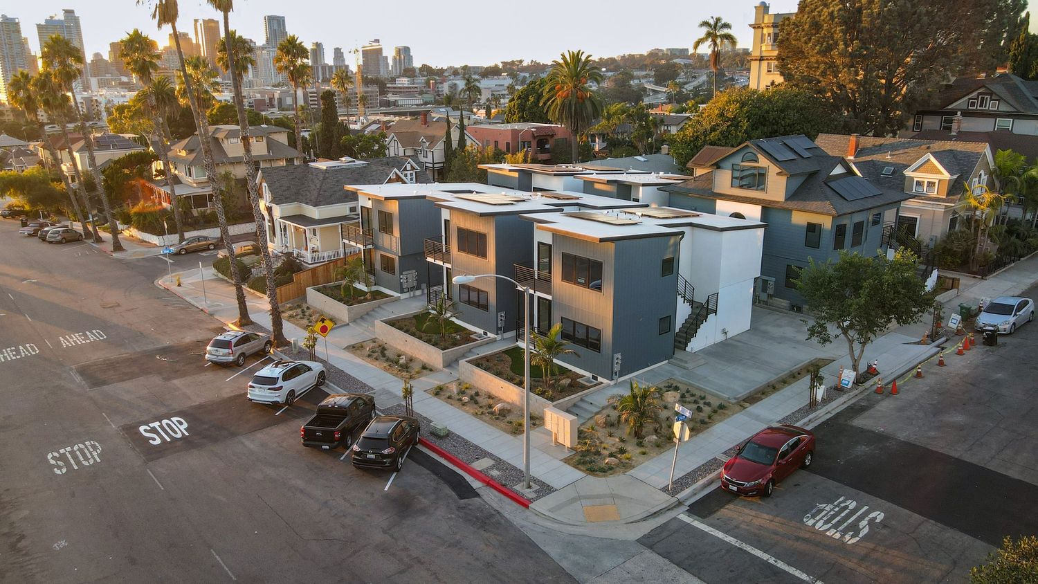 Aerial corner view of modern gray and white townhouse development near downtown San Diego skyline.