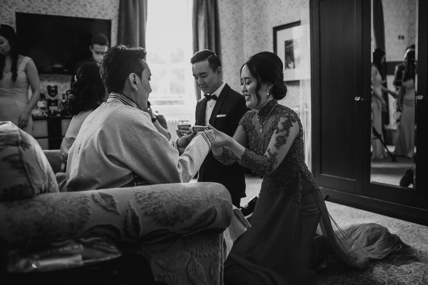 Black and white photo of a bride kneeling during a traditional Asian wedding tea ceremony.