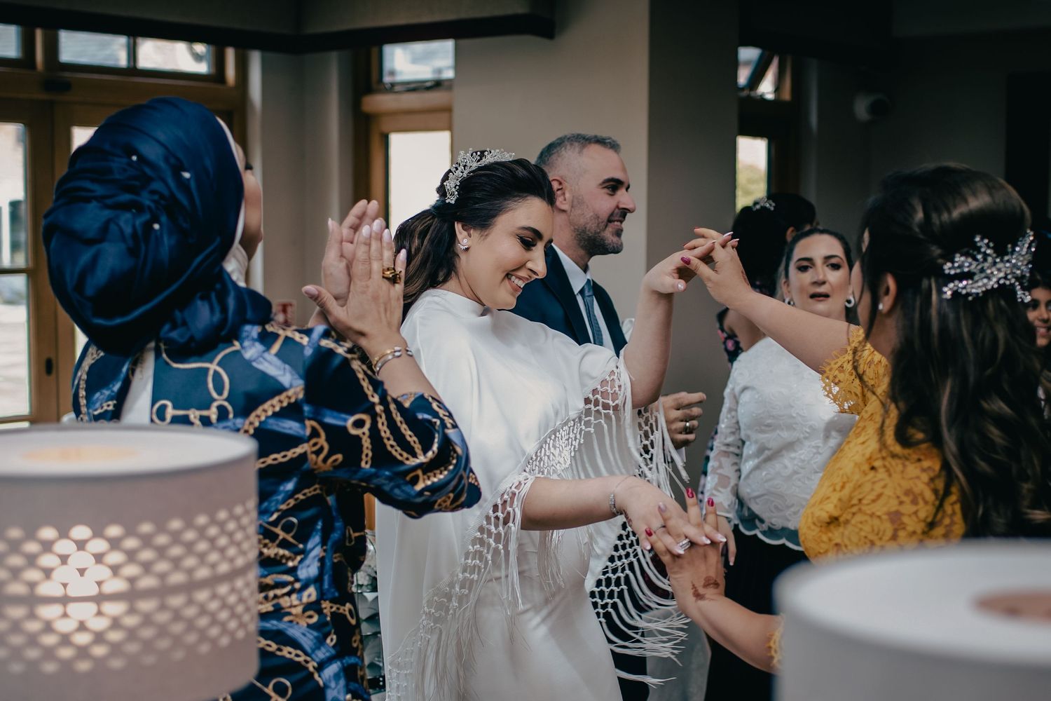 Bride in white fringed shawl celebrating with guests during lively wedding reception dance.
