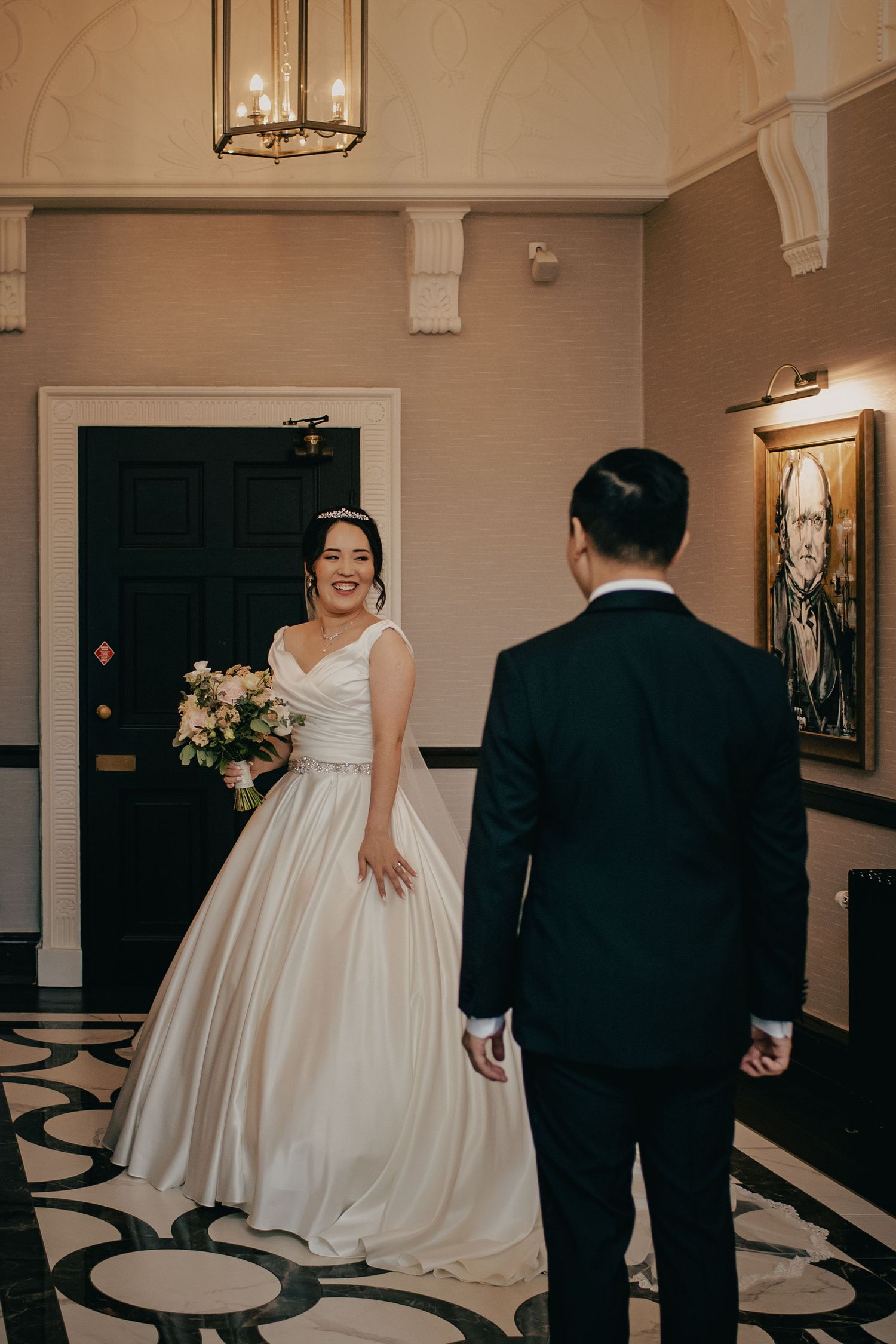 A bride in a white ballgown smiles at her groom in an elegant venue with black tile floors.