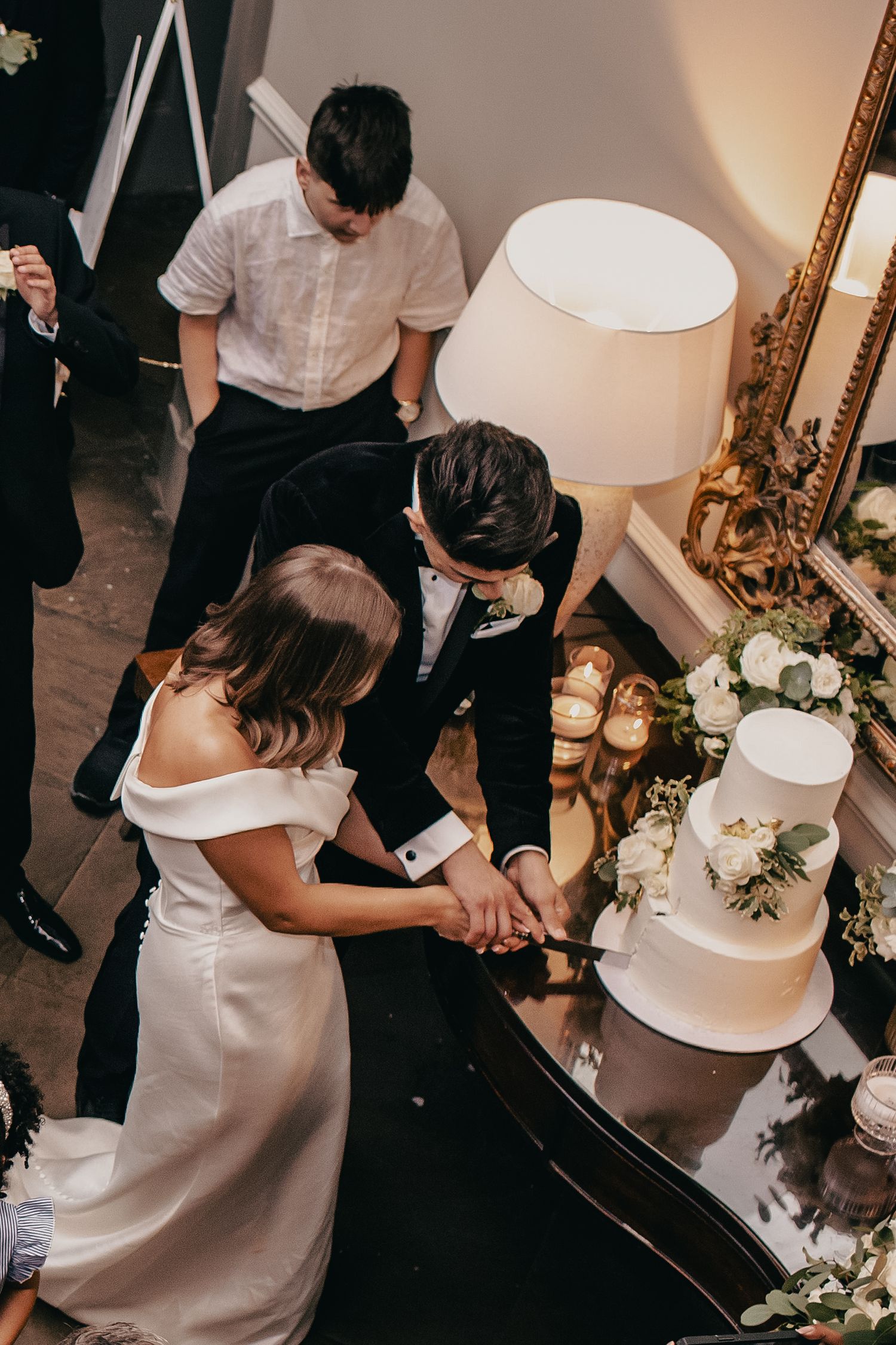 Newlyweds cut their elegant white tiered wedding cake adorned with fresh floral decorations.