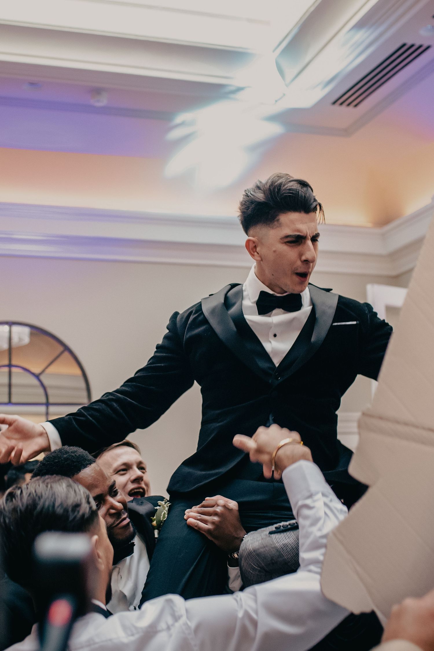 An excited groom is lifted by groomsmen during a lively wedding reception celebration.
