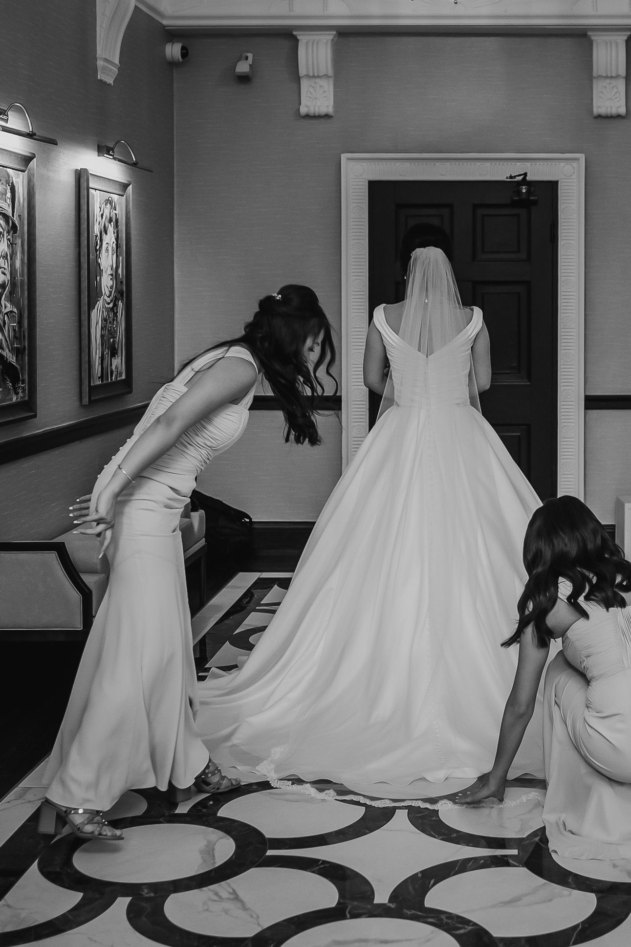 Bridesmaids adjust the train of a brides elegant white wedding gown in a classic black and white photo.