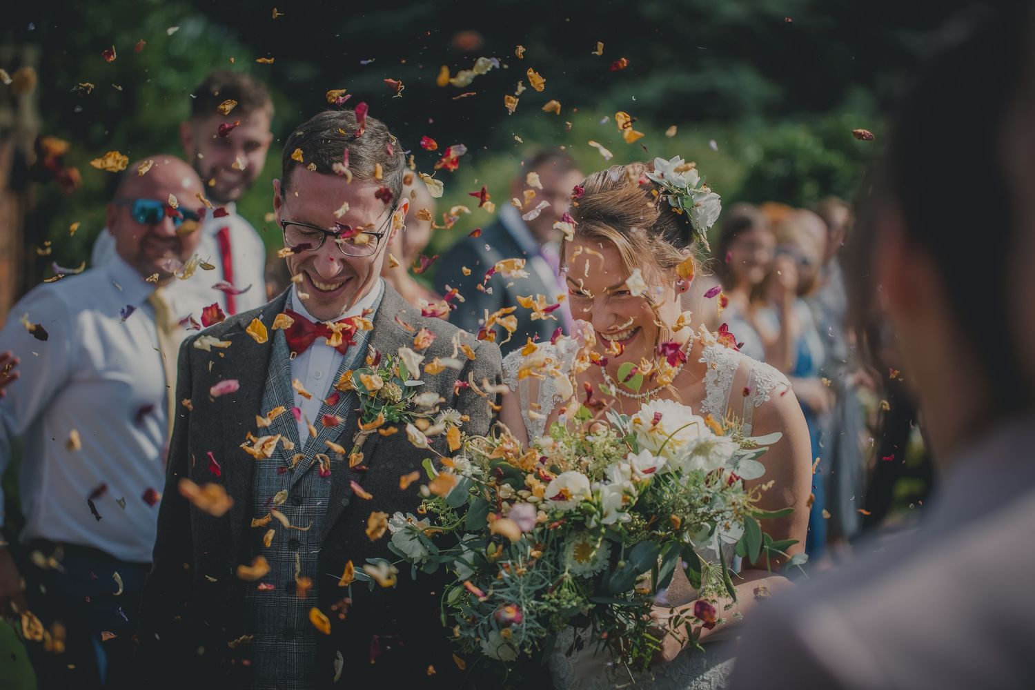Joyful newlyweds walk through colorful confetti shower surrounded by celebrating wedding guests.
