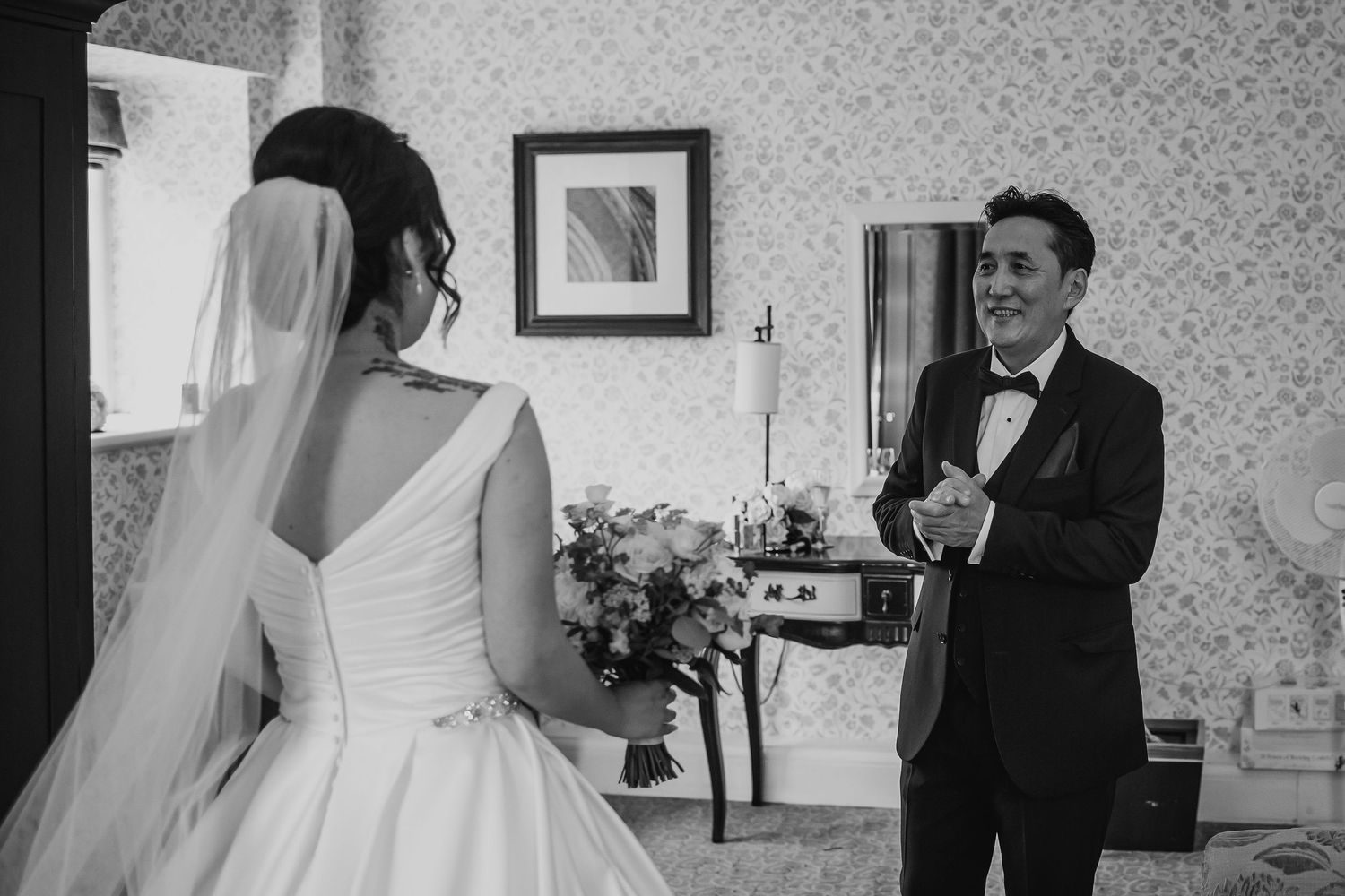 A groom smiles joyfully at his bride in a white wedding gown during their first look.