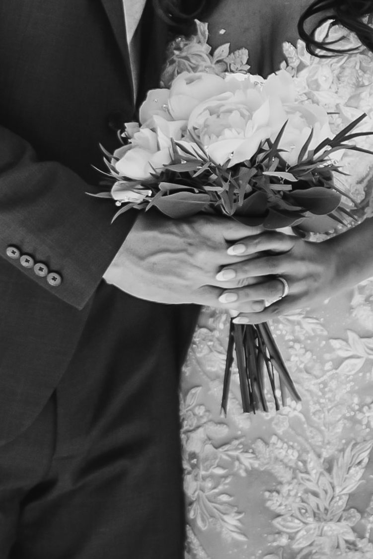 Close-up black and white photo of bride and groom holding elegant rose wedding bouquet with greenery.