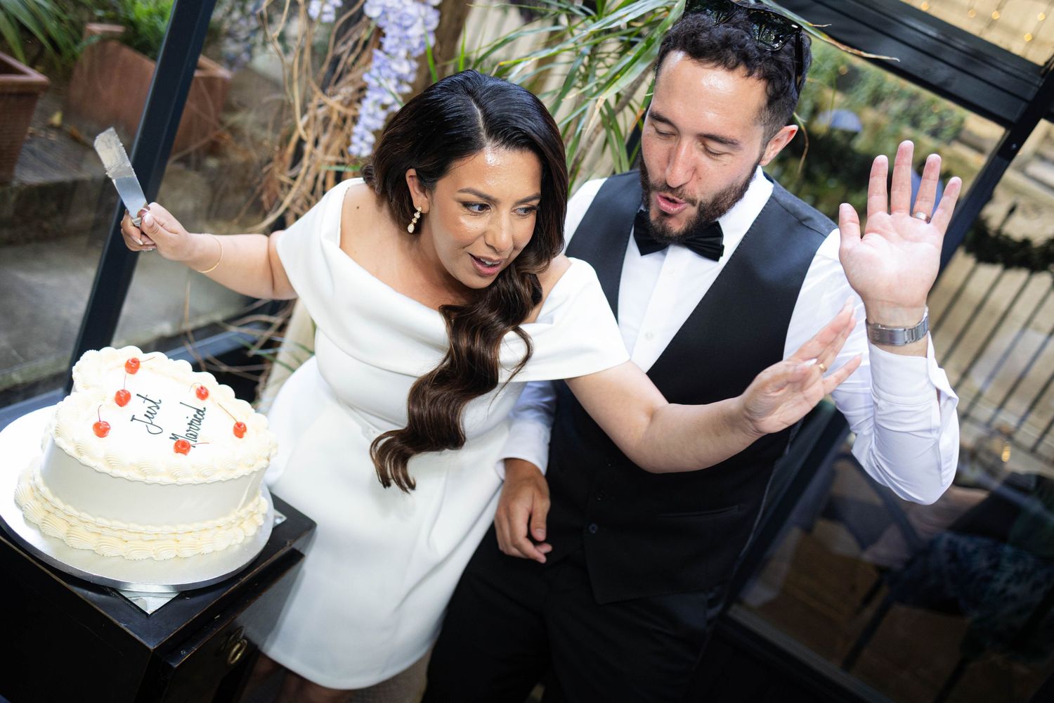 Bride and groom cutting their white wedding cake together, dressed in elegant wedding attire at a garden reception.