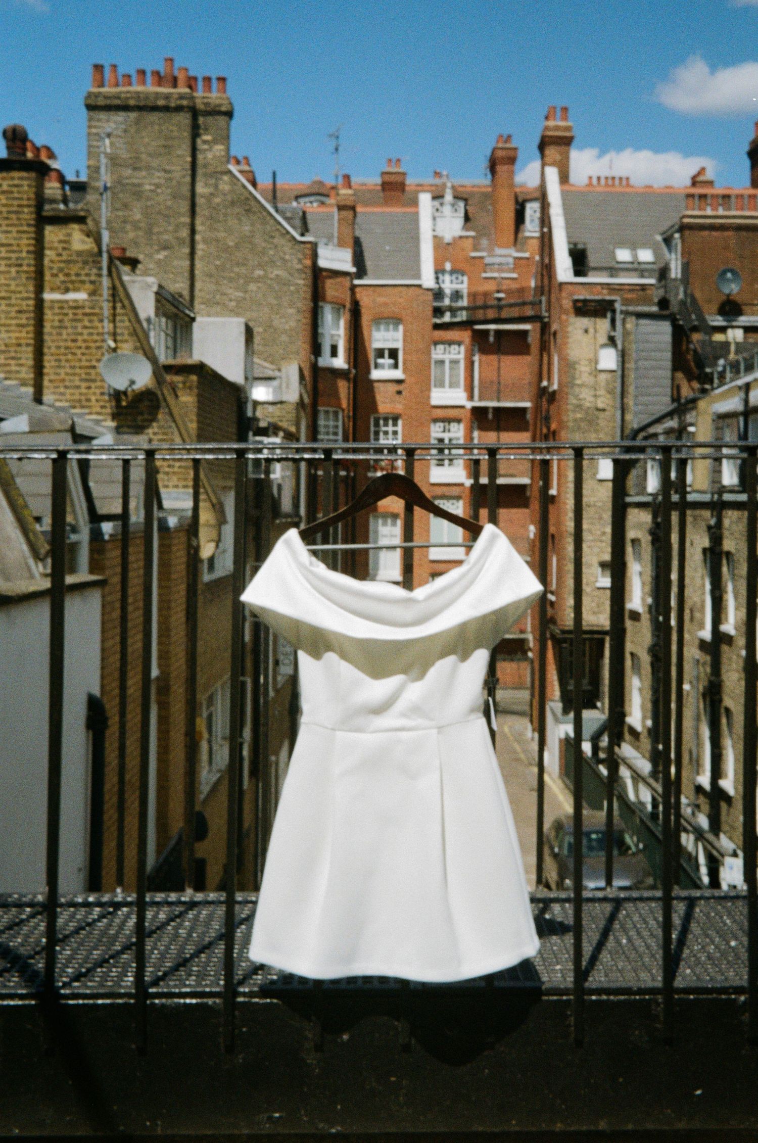 White off-shoulder mini dress hanging on a balcony railing with London brick buildings in the background.