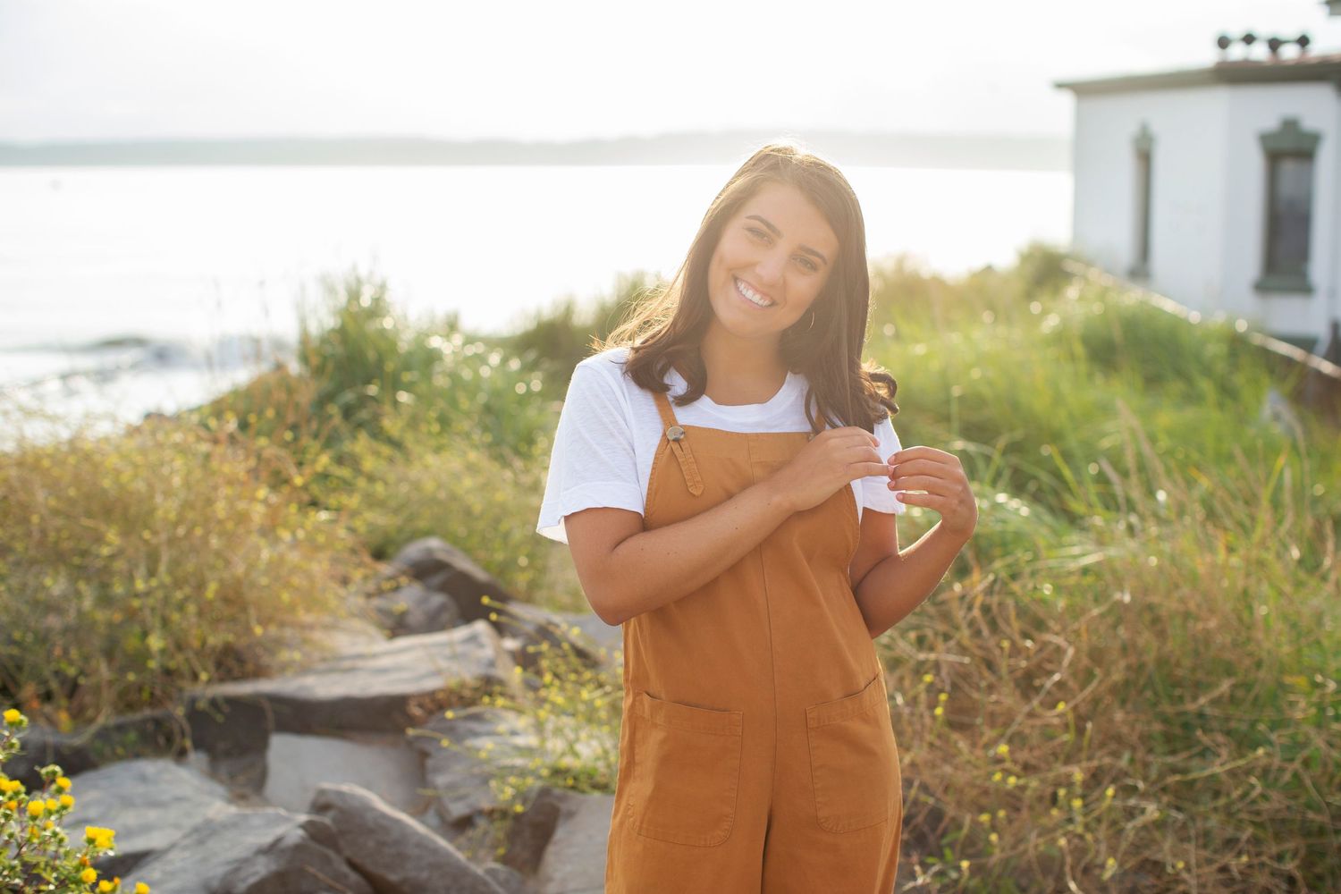 Senior Portrait girl poses with smile looking away from camera and playing with hair with summer sunset