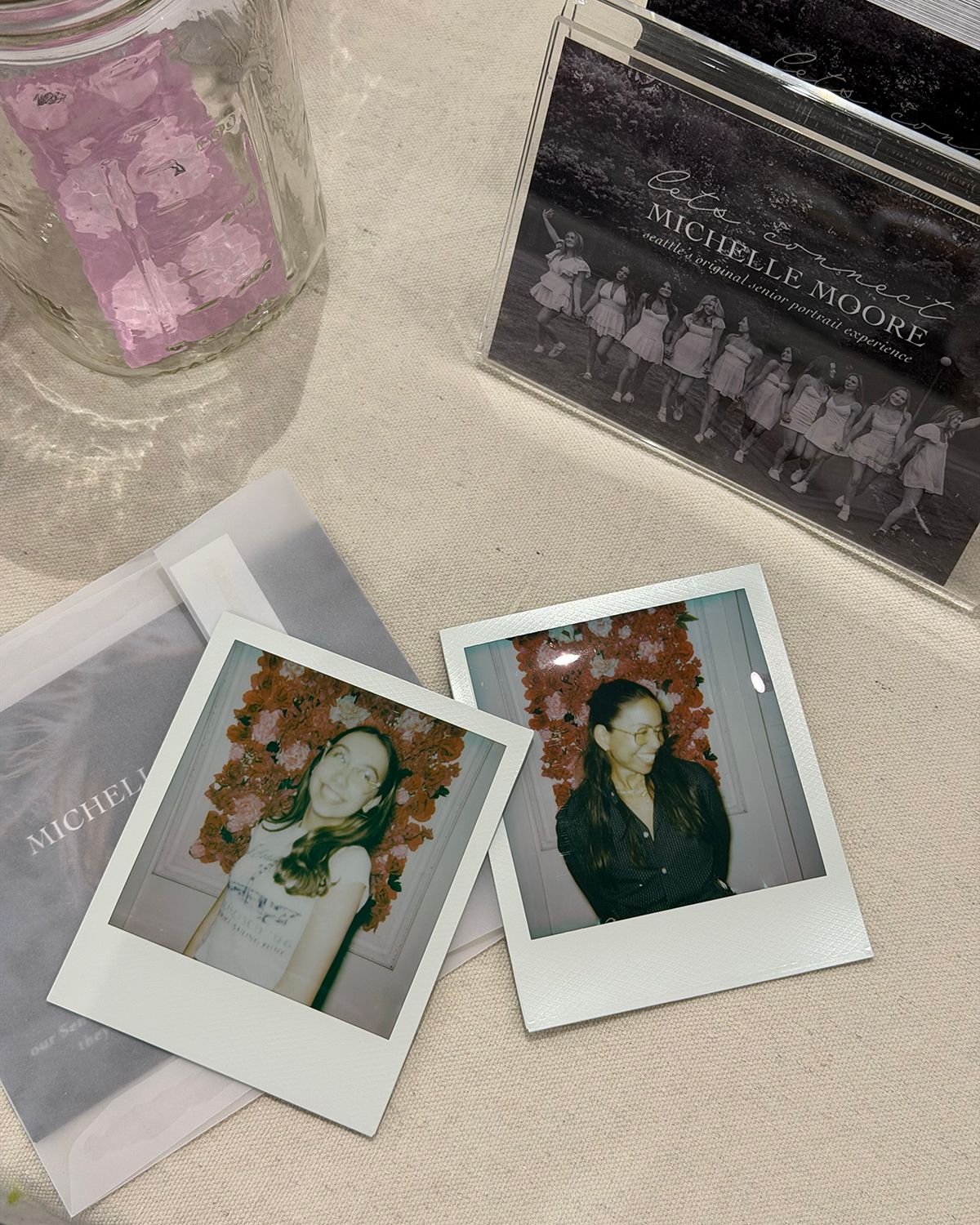 Two Polaroid photos of women displayed beside a Michelle Moore album and glass jar on a table.