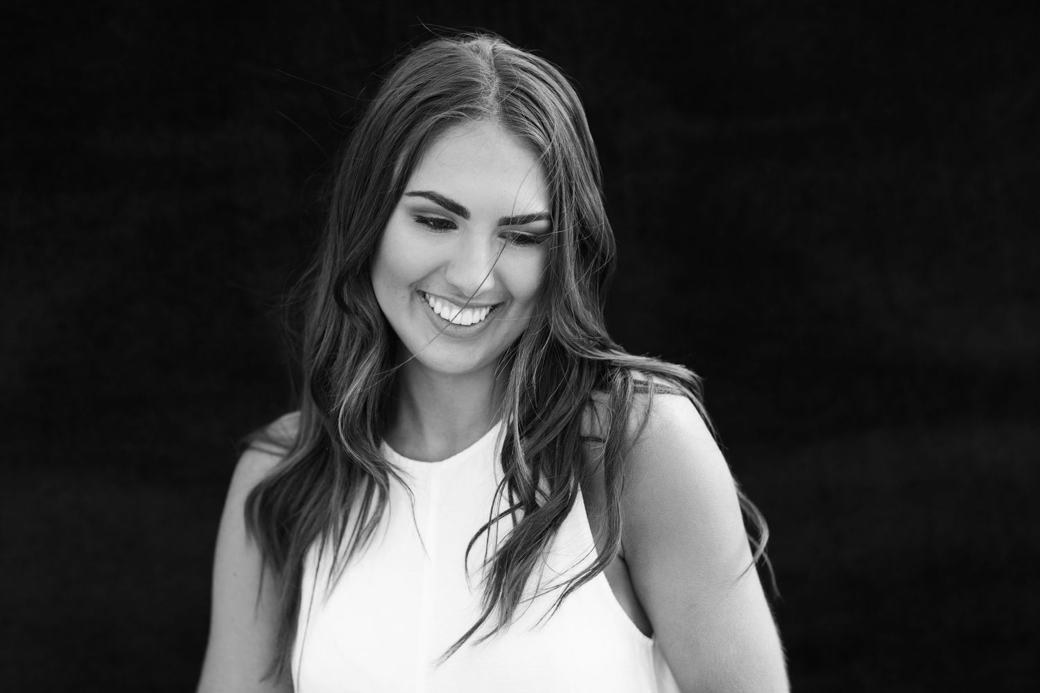 Black and white portrait of a smiling young woman with long wavy hair wearing a sleeveless white top.
