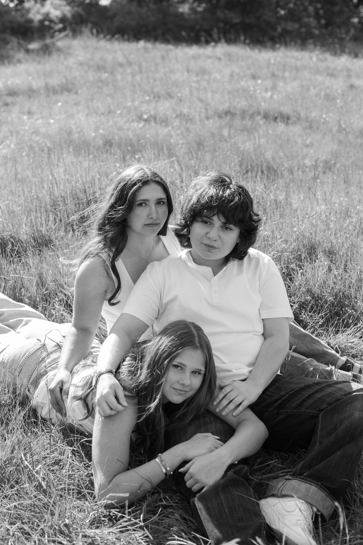 Black and white portrait of three siblings relaxing together on a grassy hillside outdoors.