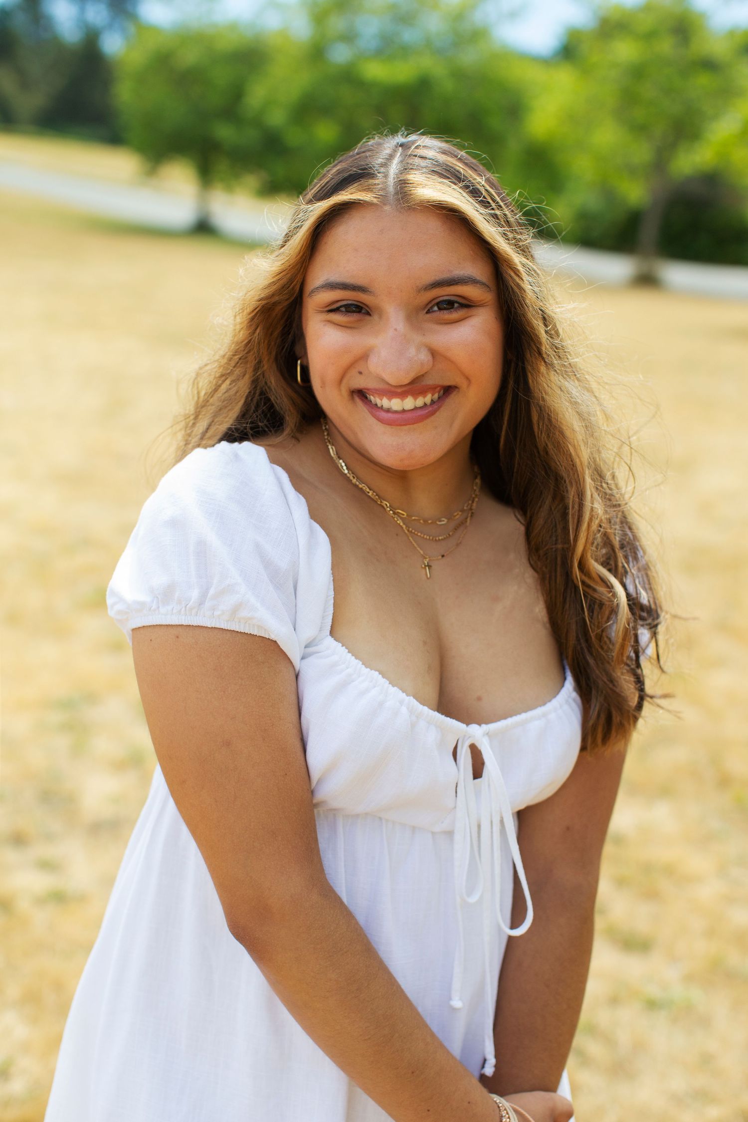 Smiling young woman in white dress posing in golden field.