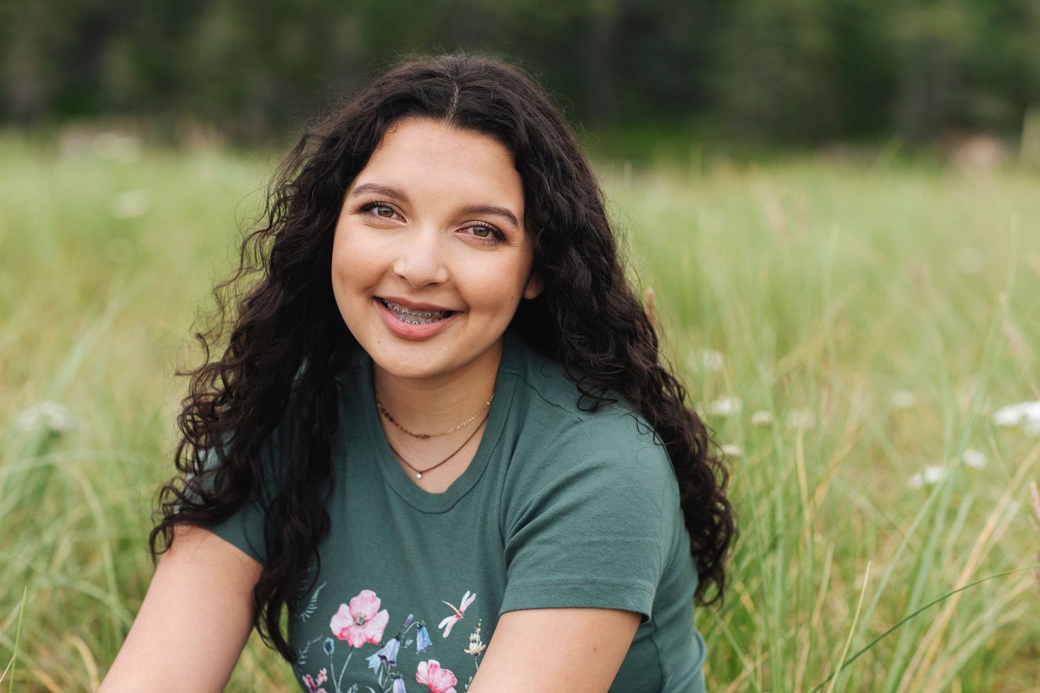 Close-up portrait of smiling young woman with curly hair in green floral tee outdoors.