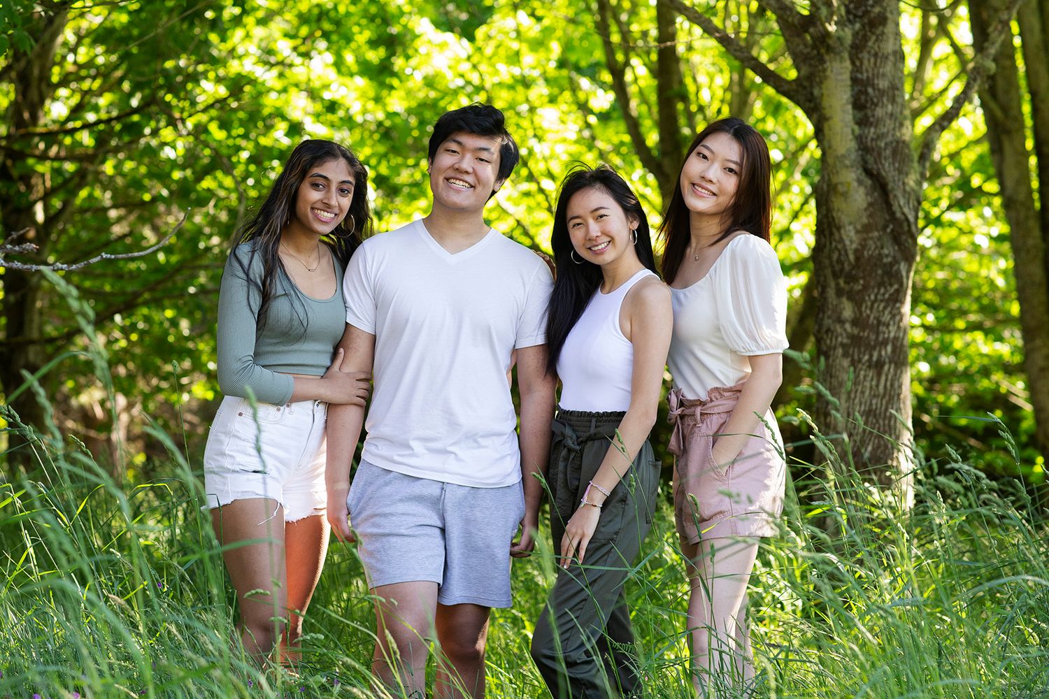 Blonde woman in white top and jeans standing in dry golden meadow with green trees.