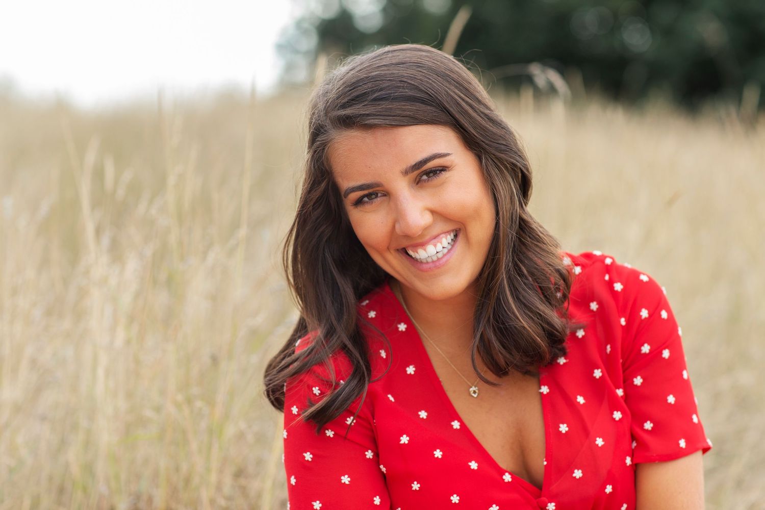 Smiling brunette woman in a red polka dot top posing in a golden wheat field.