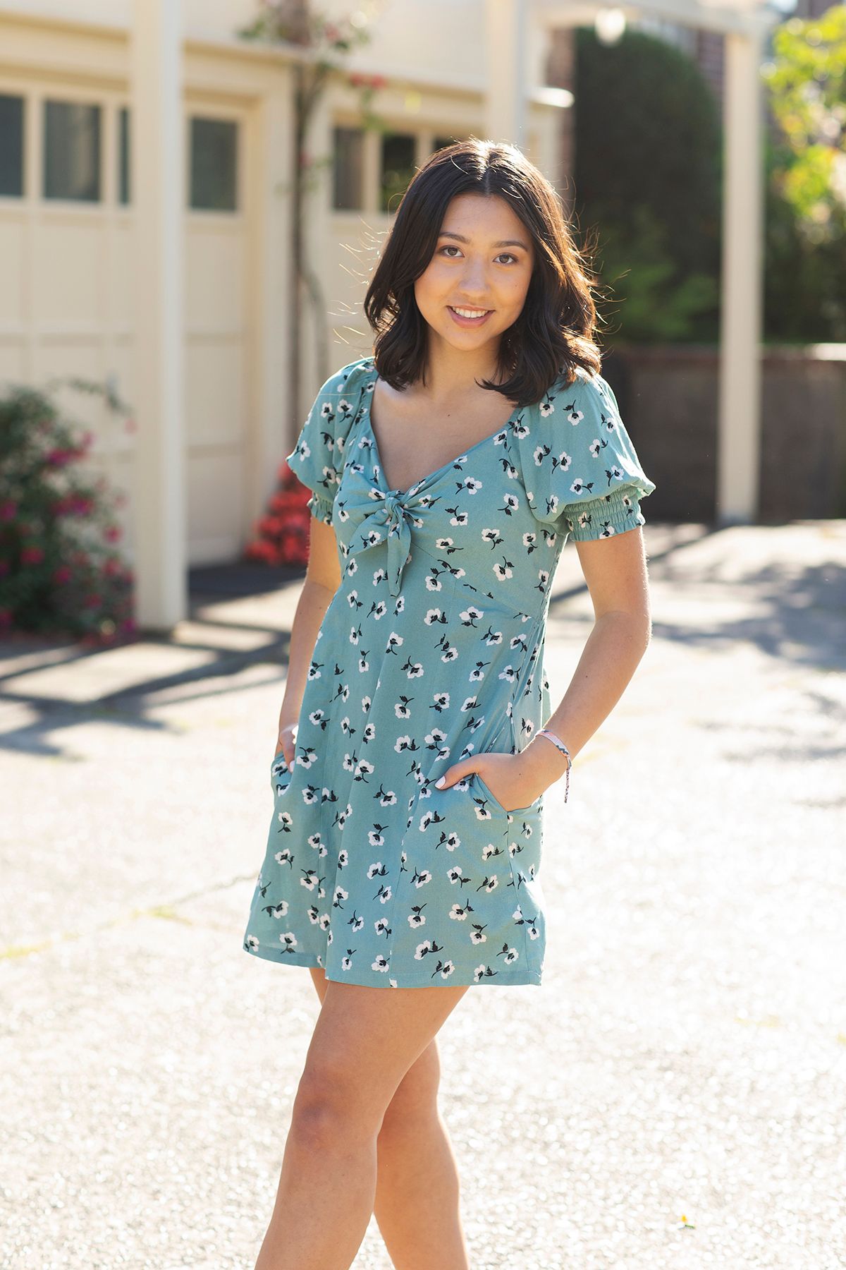 Woman in teal floral mini dress with ruffle sleeves posing outdoors on sunny day.