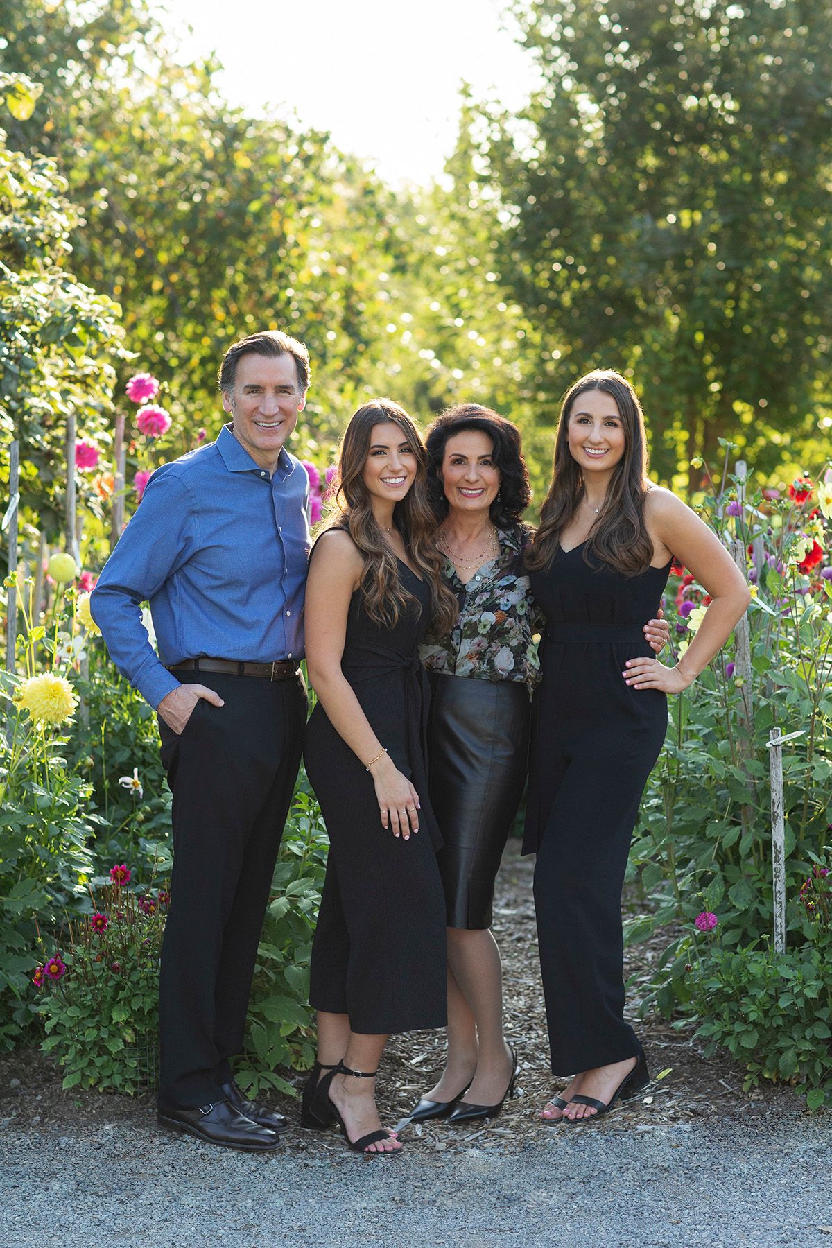 Family of four posing in a lush garden with colorful flowers, dressed in elegant dark attire for a formal portrait.