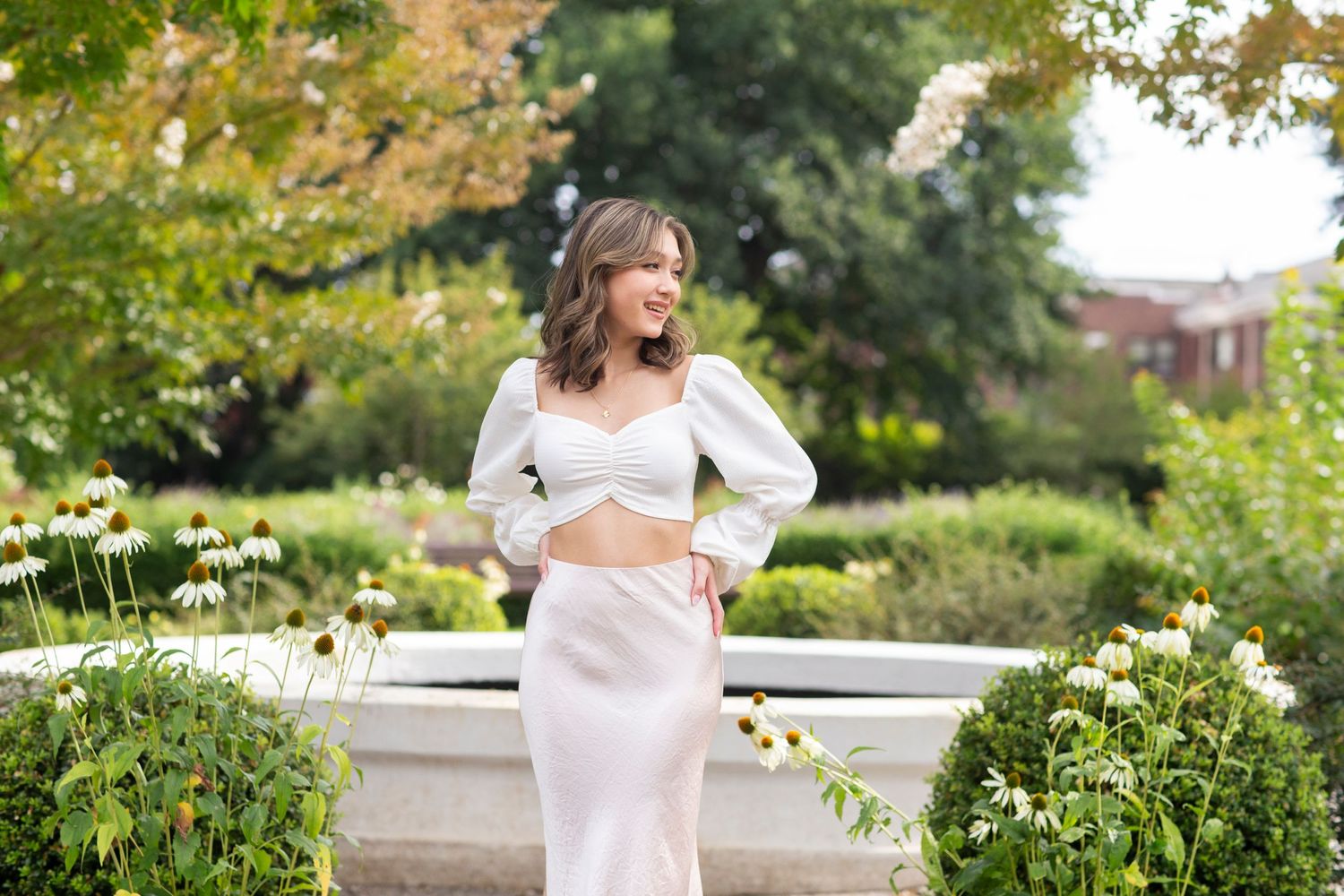 Young woman in a white two-piece crop top and satin skirt set laughing in a sunny garden setting.
