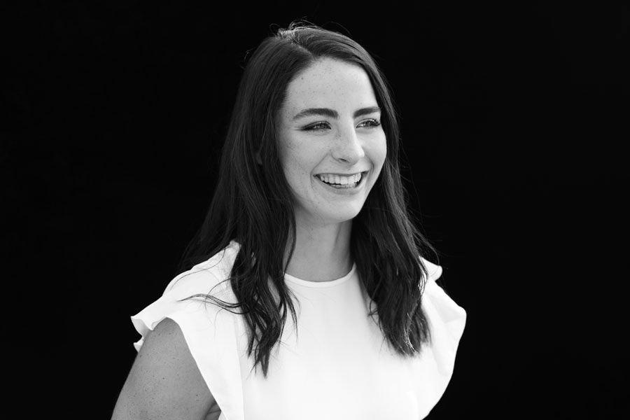 Black and white portrait of a smiling young woman with dark hair wearing a white ruffled top.