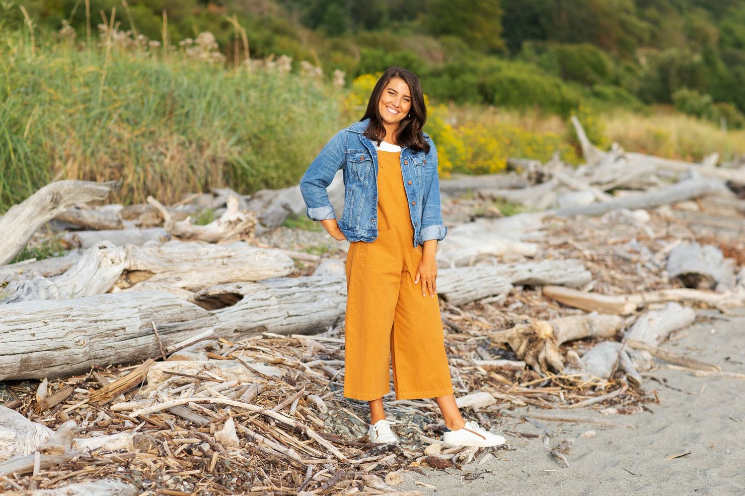 Senior Portrait girl wearing orange overalls and denim jacket with discovery park driftwood beach in background