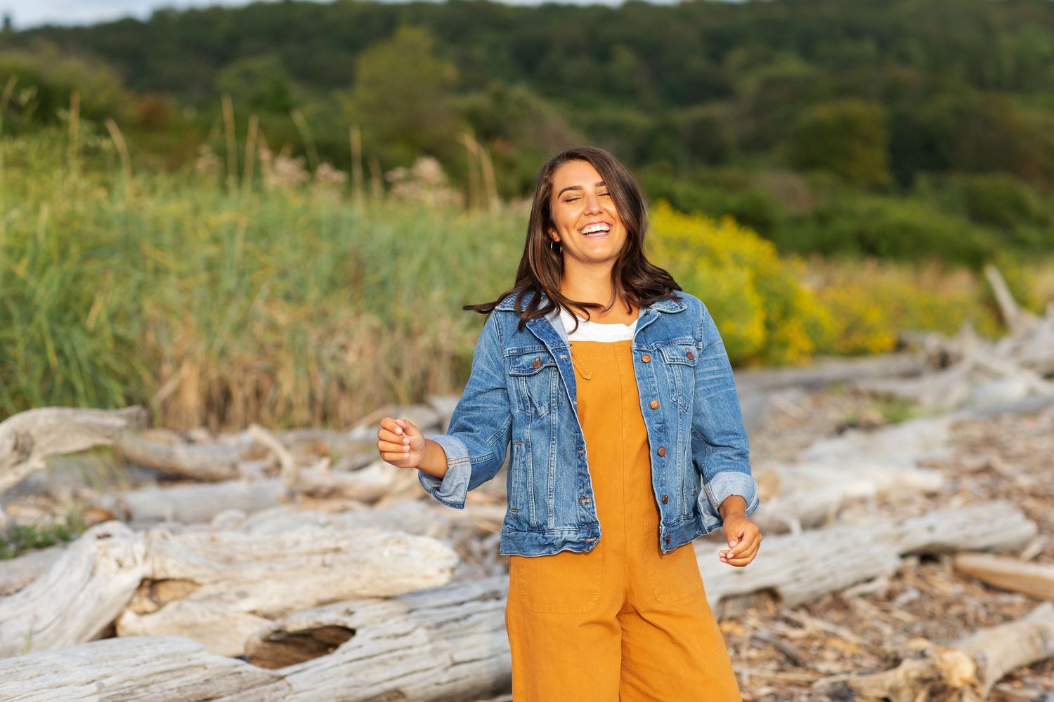 Senior Portrait girl wearing orange overalls and denim jacket with discovery park driftwood beach in background