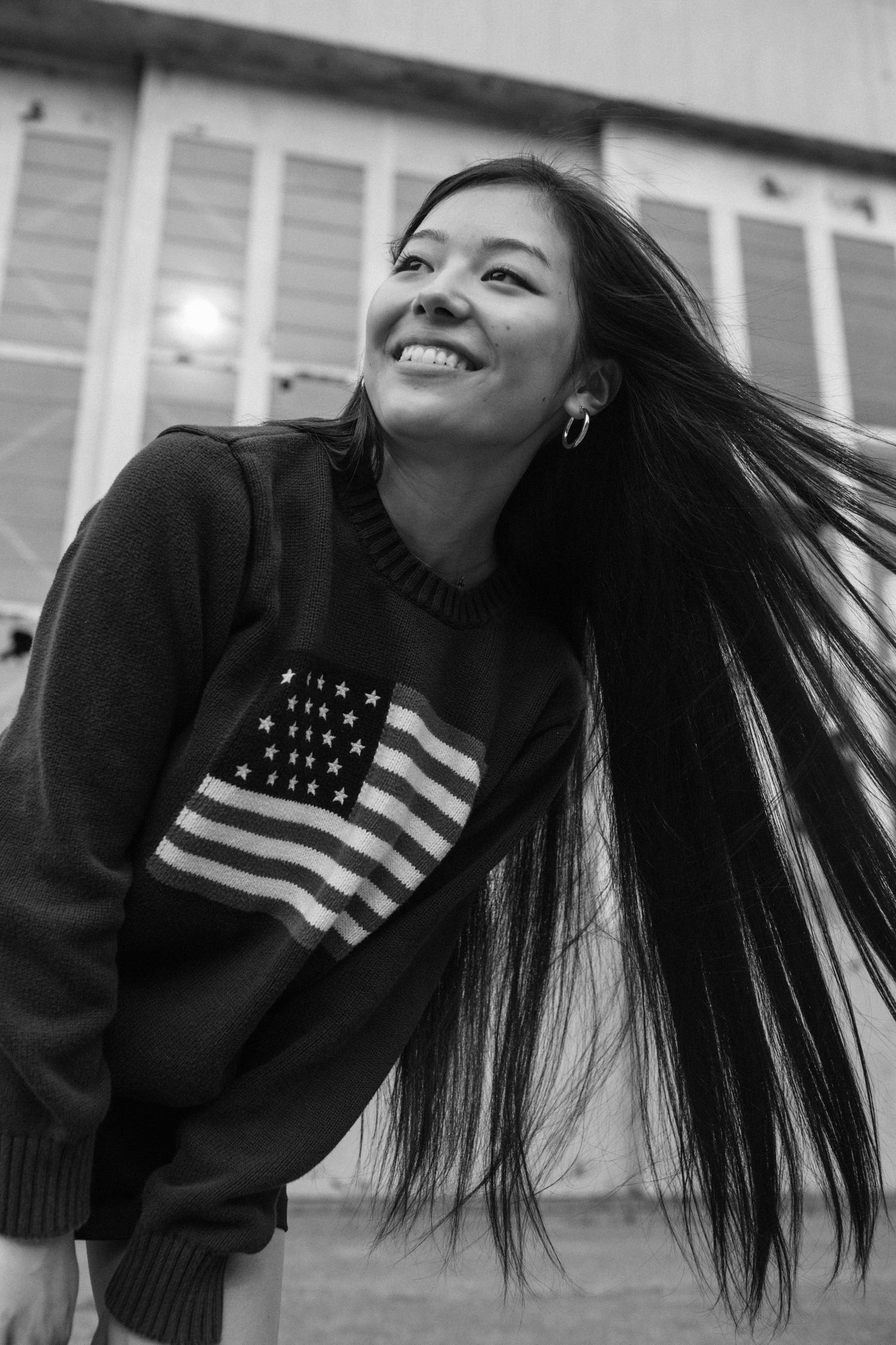 Smiling young woman with long flowing dark hair wearing American flag sweater in black and white.