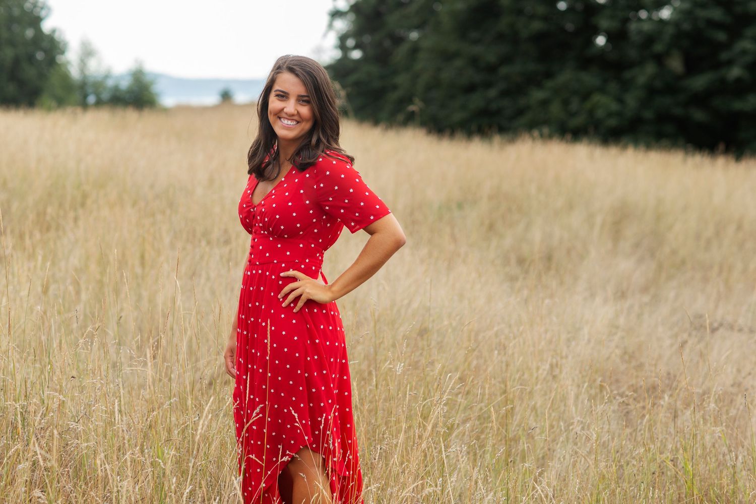 Woman in red polka dot dress posing in tall golden grass field.