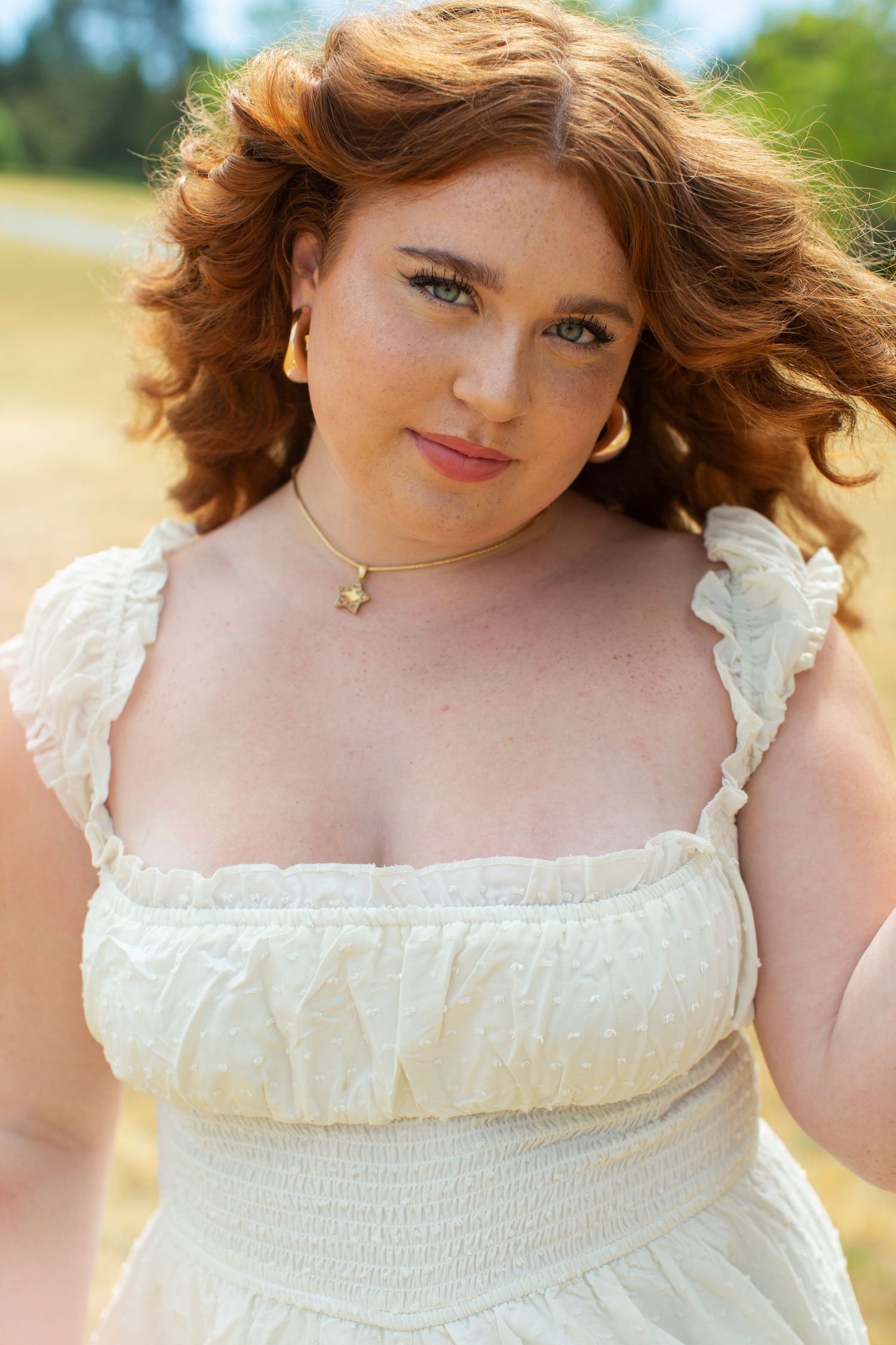 Young redhead woman in cream dress with gold necklace outdoors.