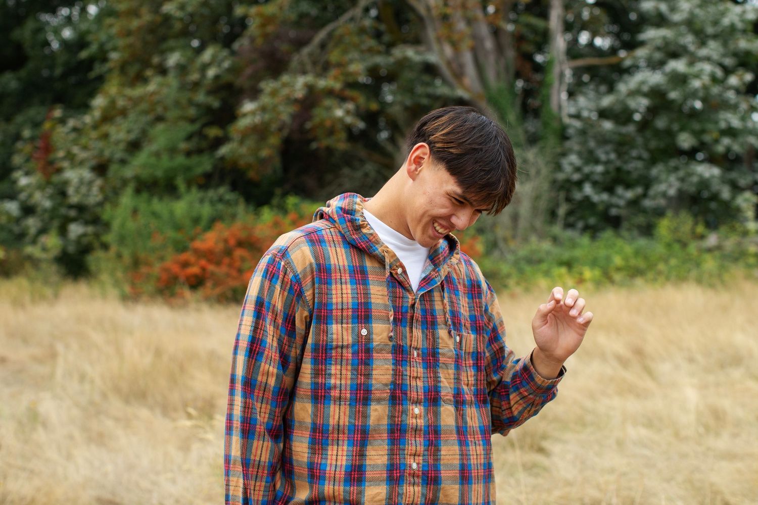 Young man in plaid flannel laughing while standing in golden meadow outdoors.