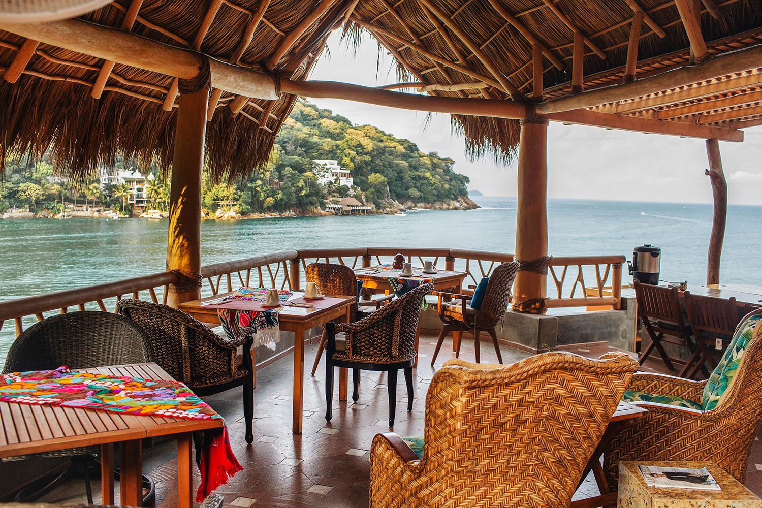 Open-air palapa restaurant with wicker chairs overlooking turquoise ocean bay in a tropical Mexican resort.