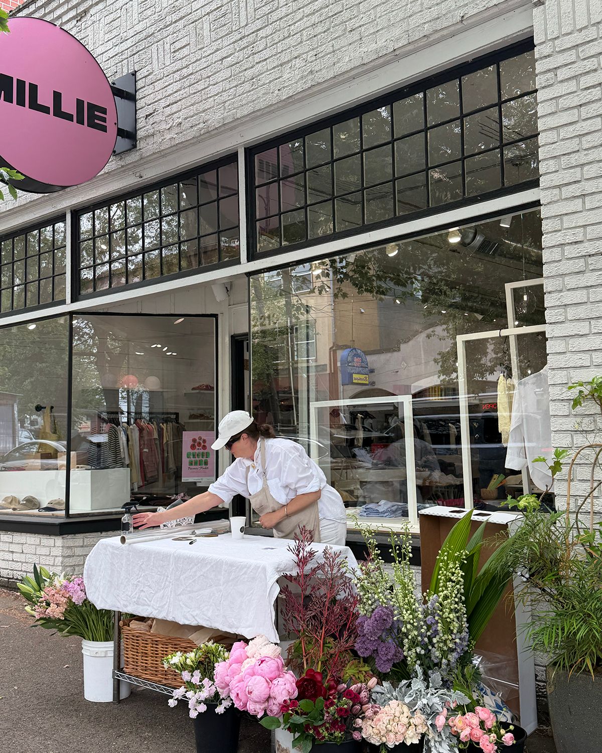 Florist arranging flowers outside Millie shop with white linen table and colorful blooms on a sunny day.