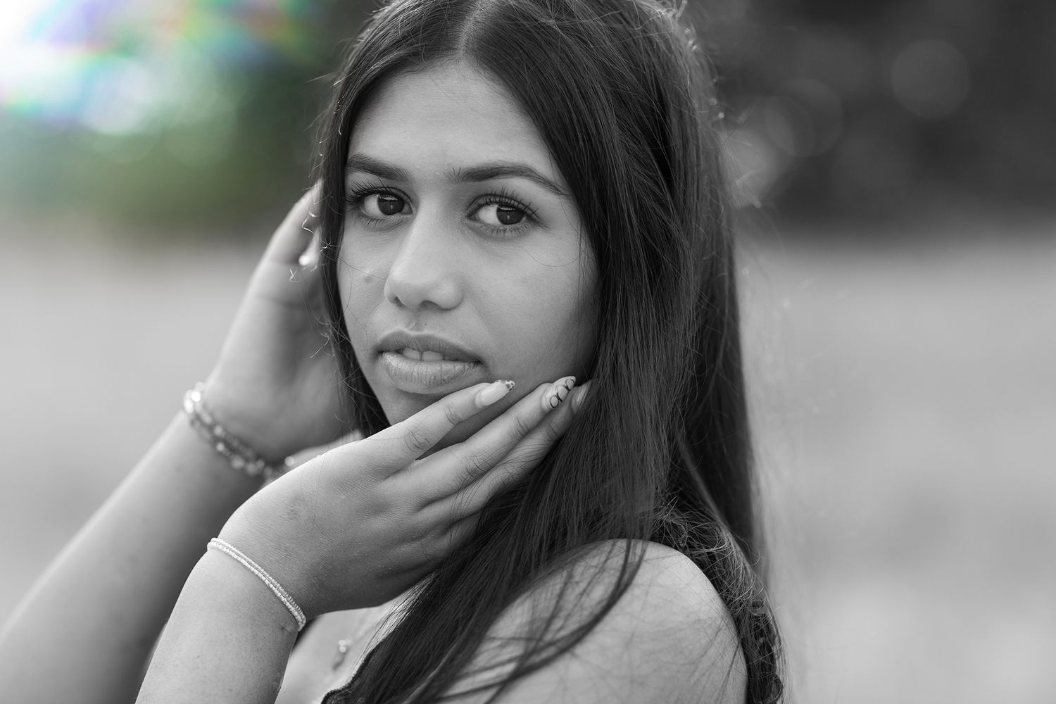 Black and white close-up portrait of young woman with long dark hair touching her face.