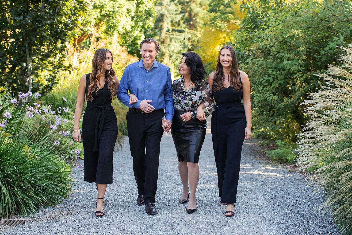 Four elegantly dressed people walking together on a garden path surrounded by lush greenery.