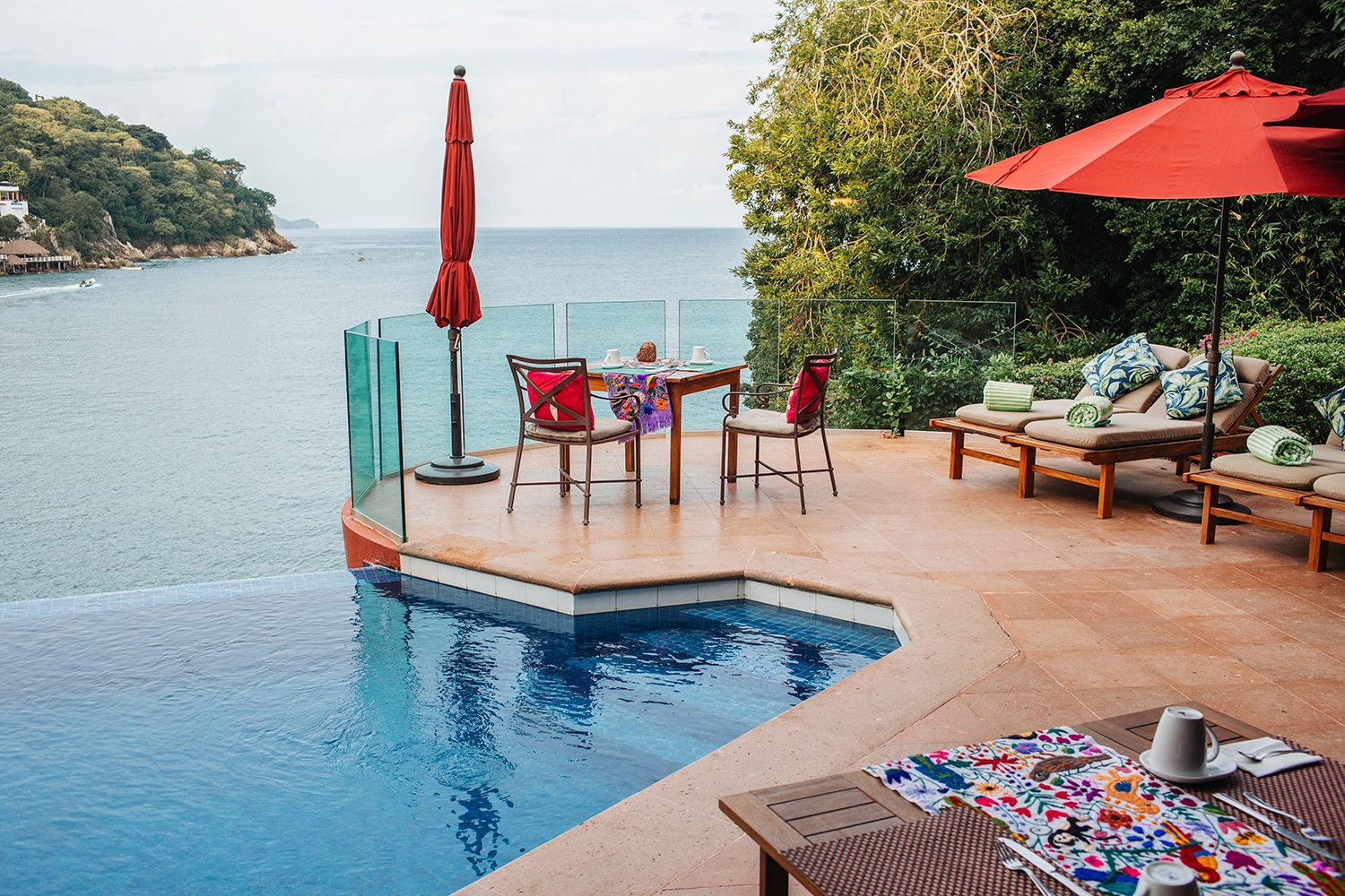 Luxury infinity pool terrace with red umbrellas, lounge chairs, and stunning ocean view in a tropical resort.
