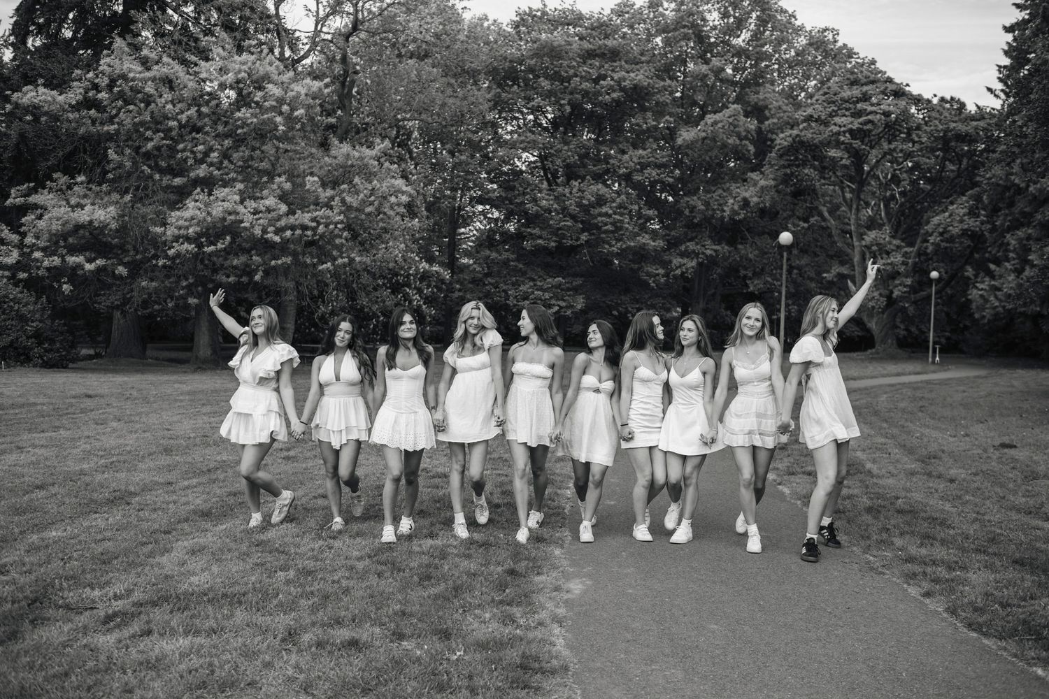 Black and white photo of a group of women in white dresses walking together in a park.