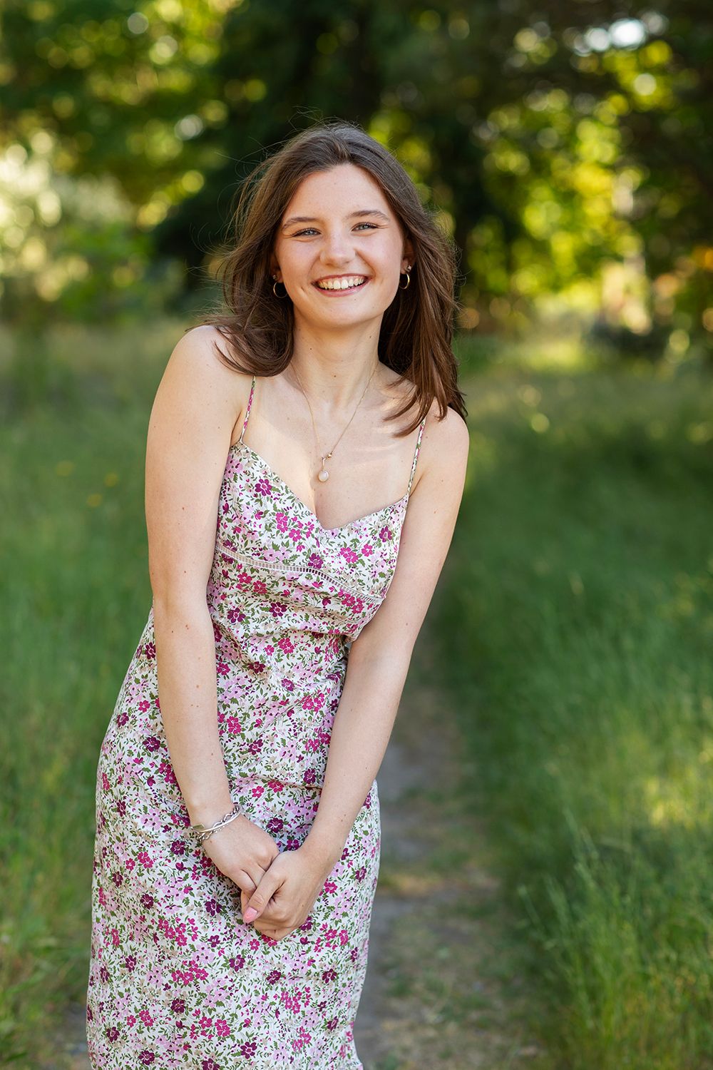 Young woman in floral sundress smiling outdoors on a green nature path in summer.