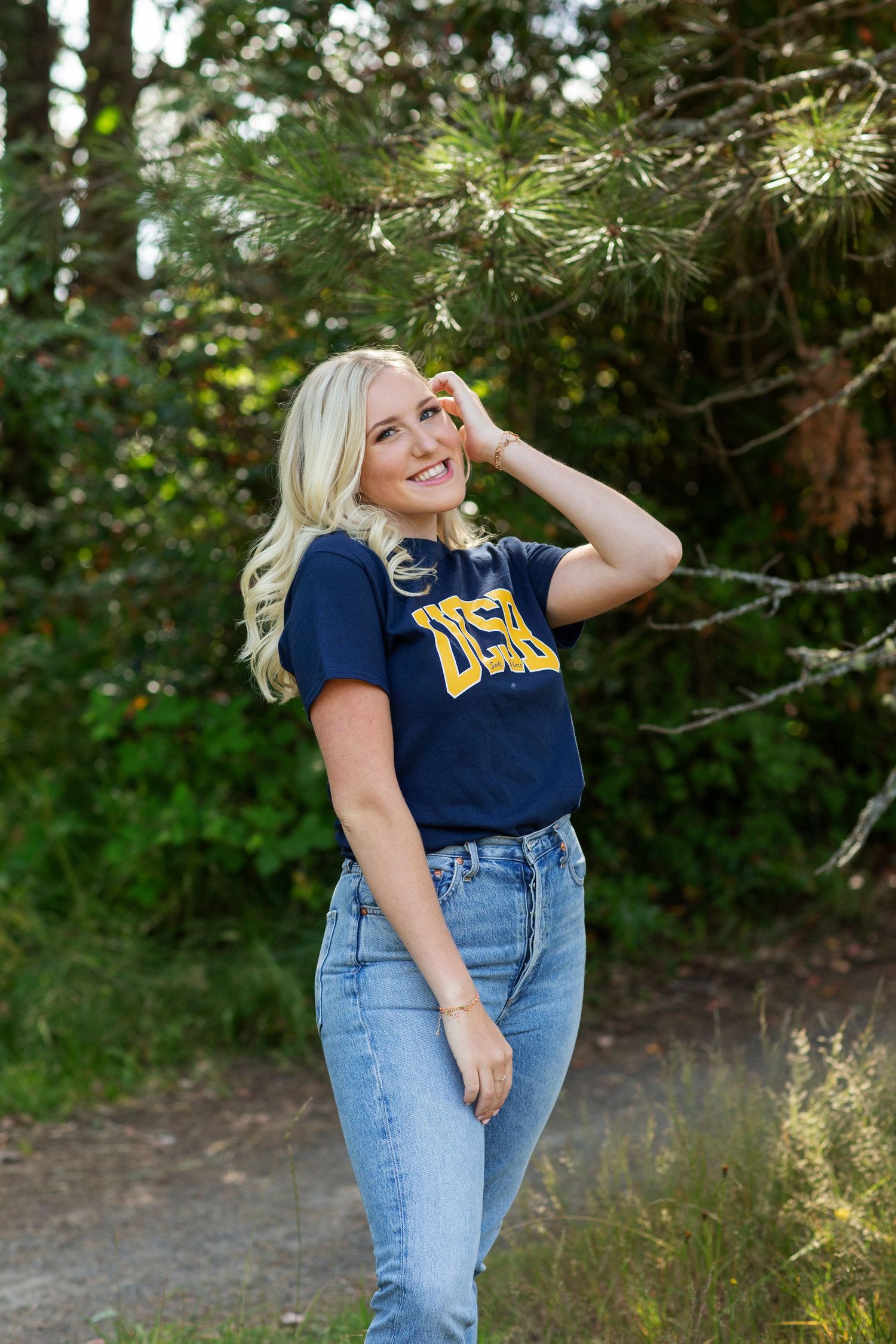 Smiling blonde woman in a navy UCSB shirt and high-waist jeans posing on an outdoor trail.