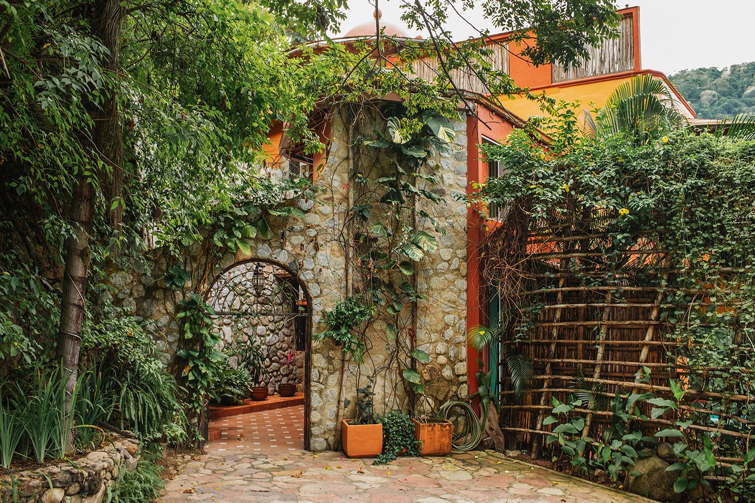 Lush green ivy-covered stone archway entrance with terracotta pots in a charming Mexican garden courtyard.