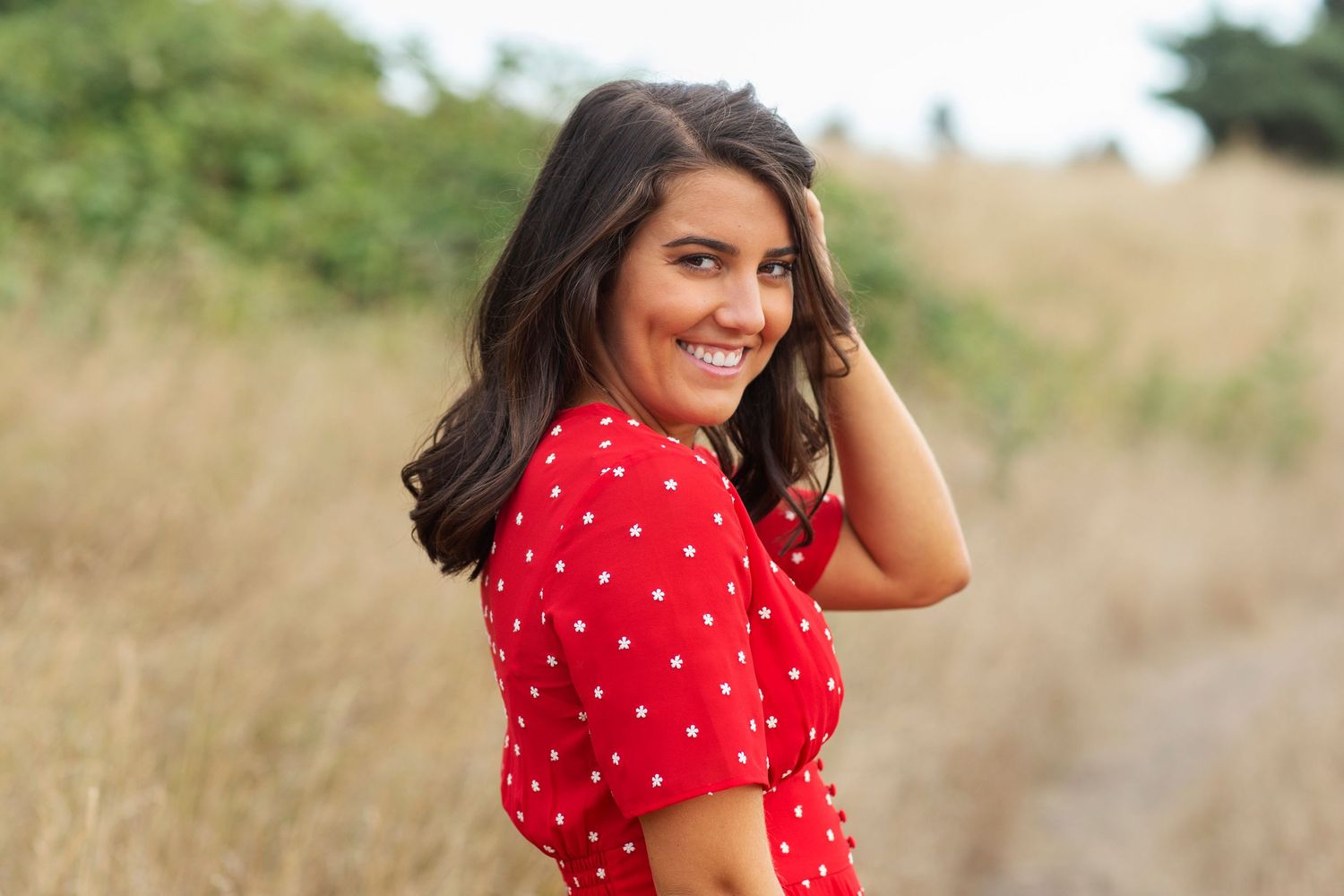 Smiling brunette woman in red dress looking back over shoulder.
