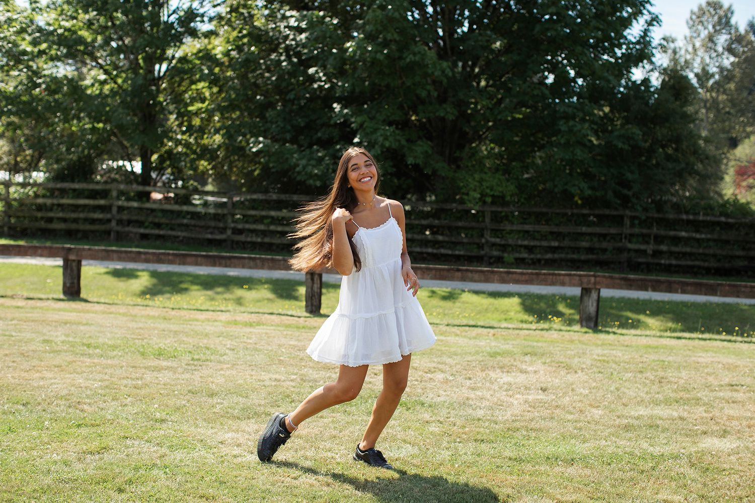 Young woman in white sundress and black shoes twirling joyfully on green grass in a sunny park.