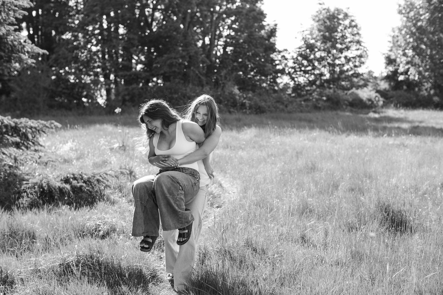 Two girls playing in a grassy meadow with trees, captured in black and white photography.